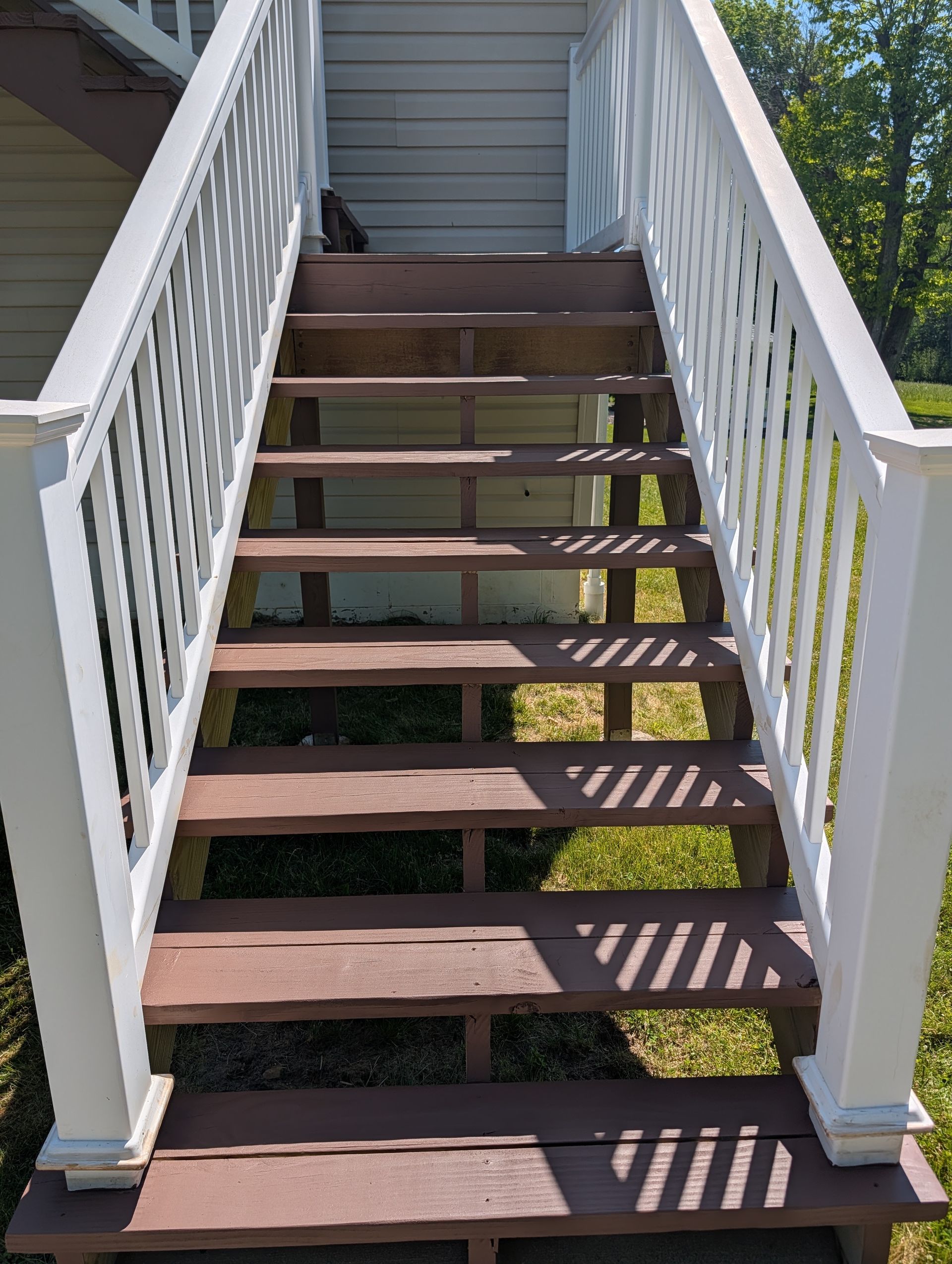 Outdoor wooden staircase with white railings leading up to a gray house