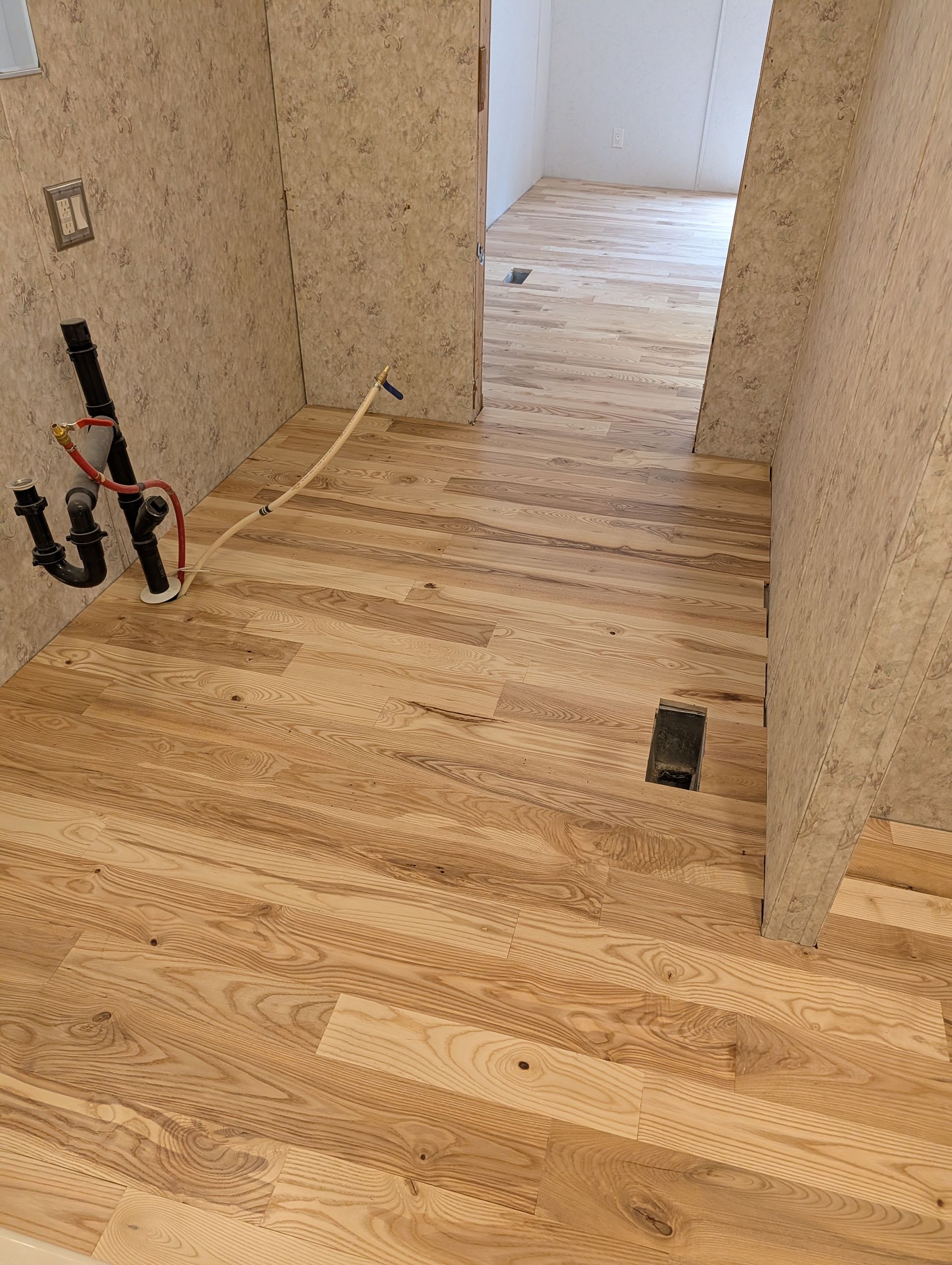 Unfinished hallway with light wood flooring and exposed wiring on beige walls.