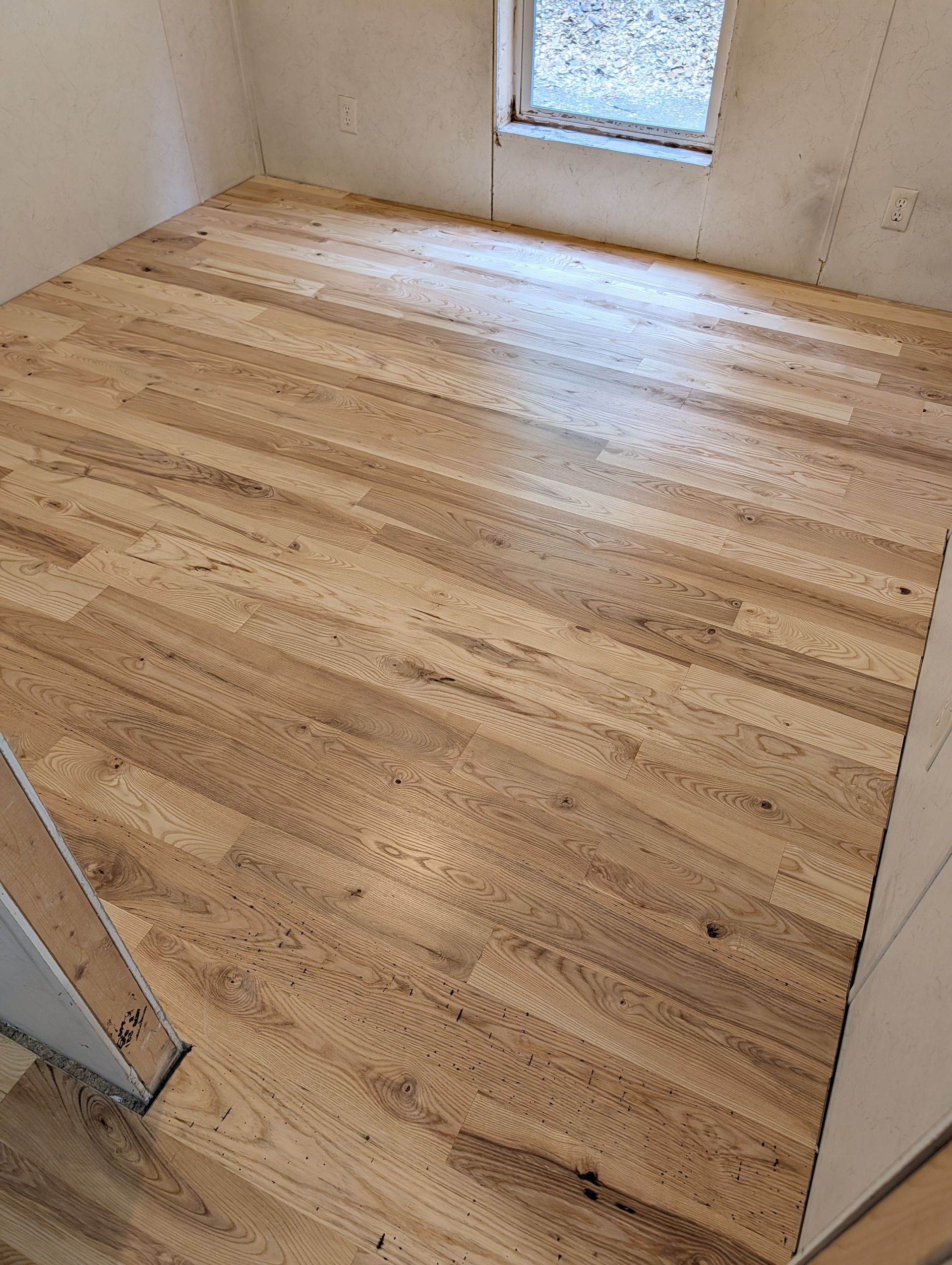 Small empty room with light wood flooring and a small window on the far wall.