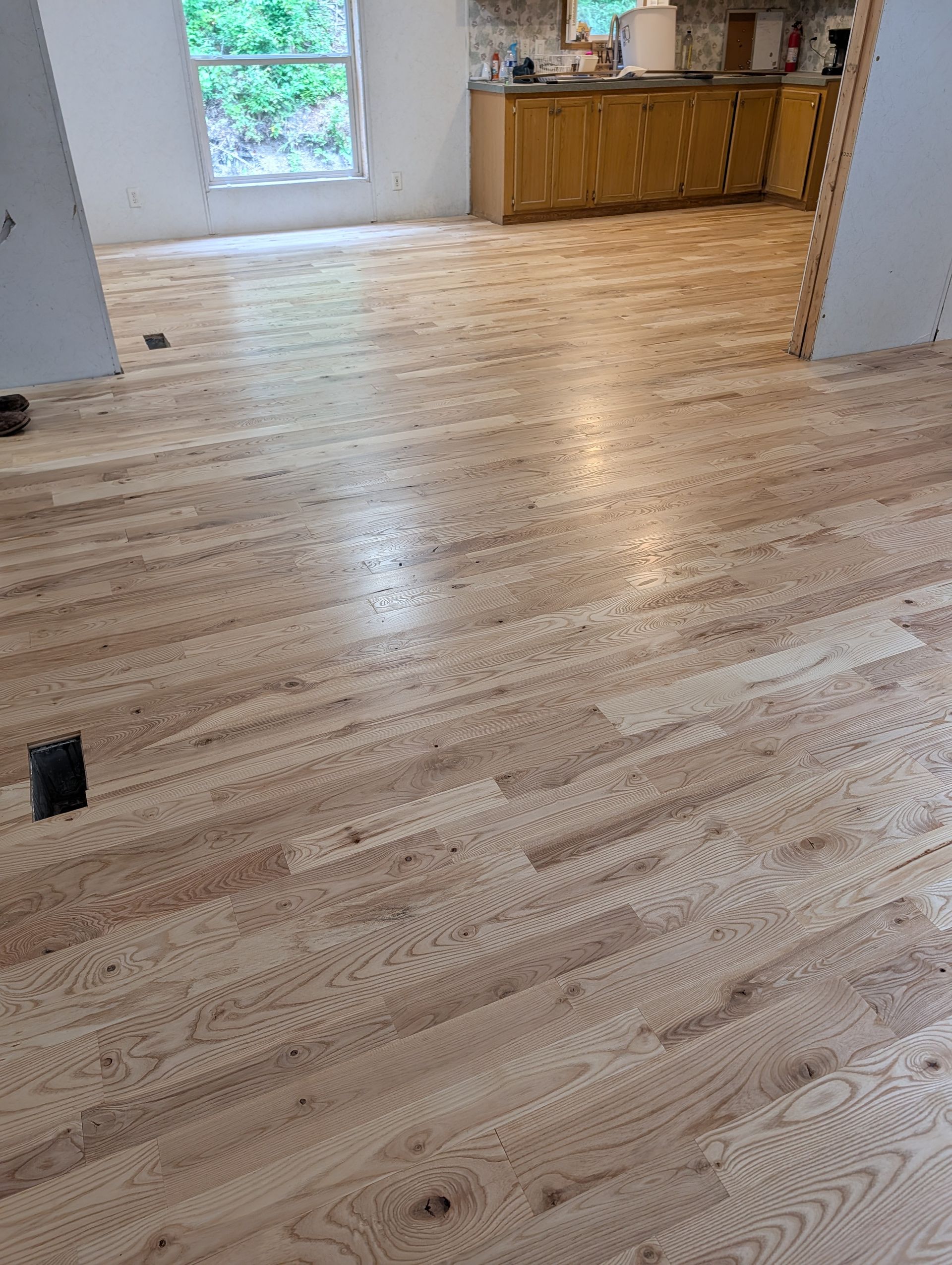 Freshly finished light wood floor in an empty room with a window and a wooden cabinet in back