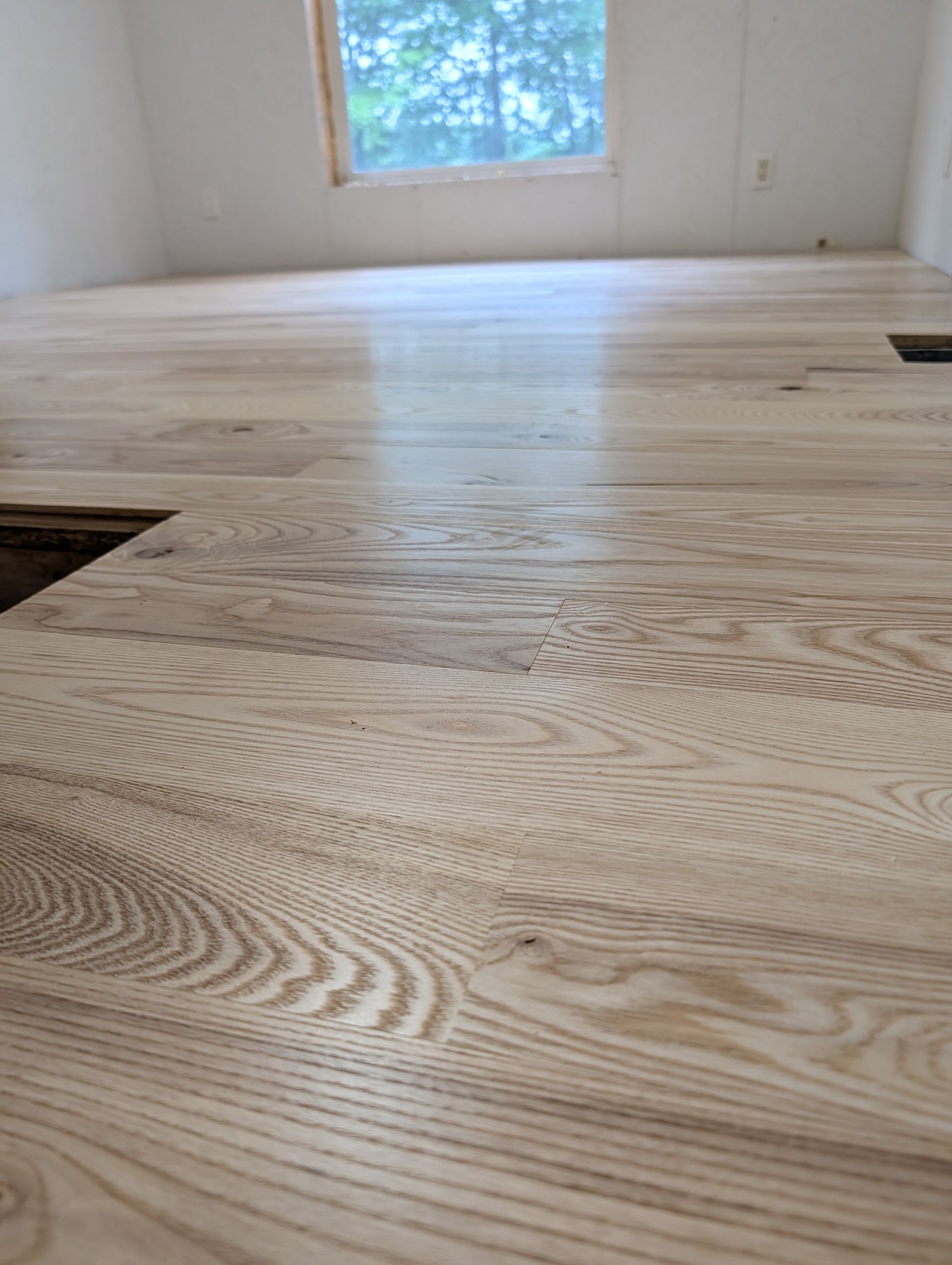 Freshly sanded hardwood floor in an empty room with a window in the background