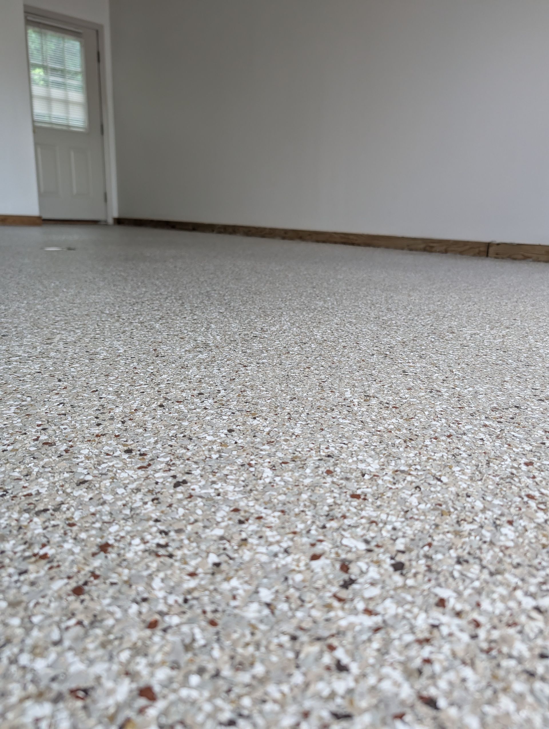 Empty room with speckled carpet, white walls, wood baseboards, and a door with a window.