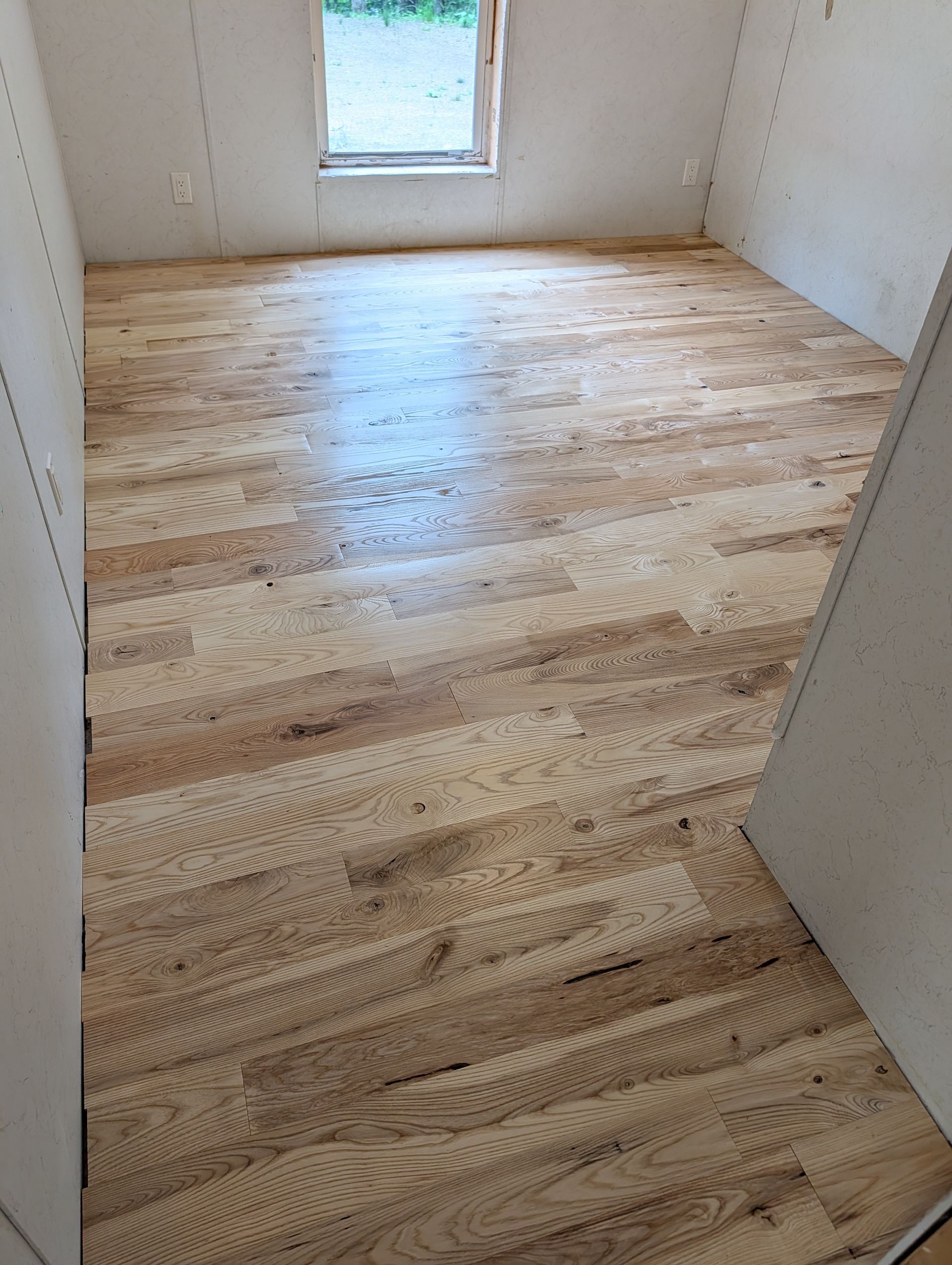 Empty room with light wood floor and small window in white walls