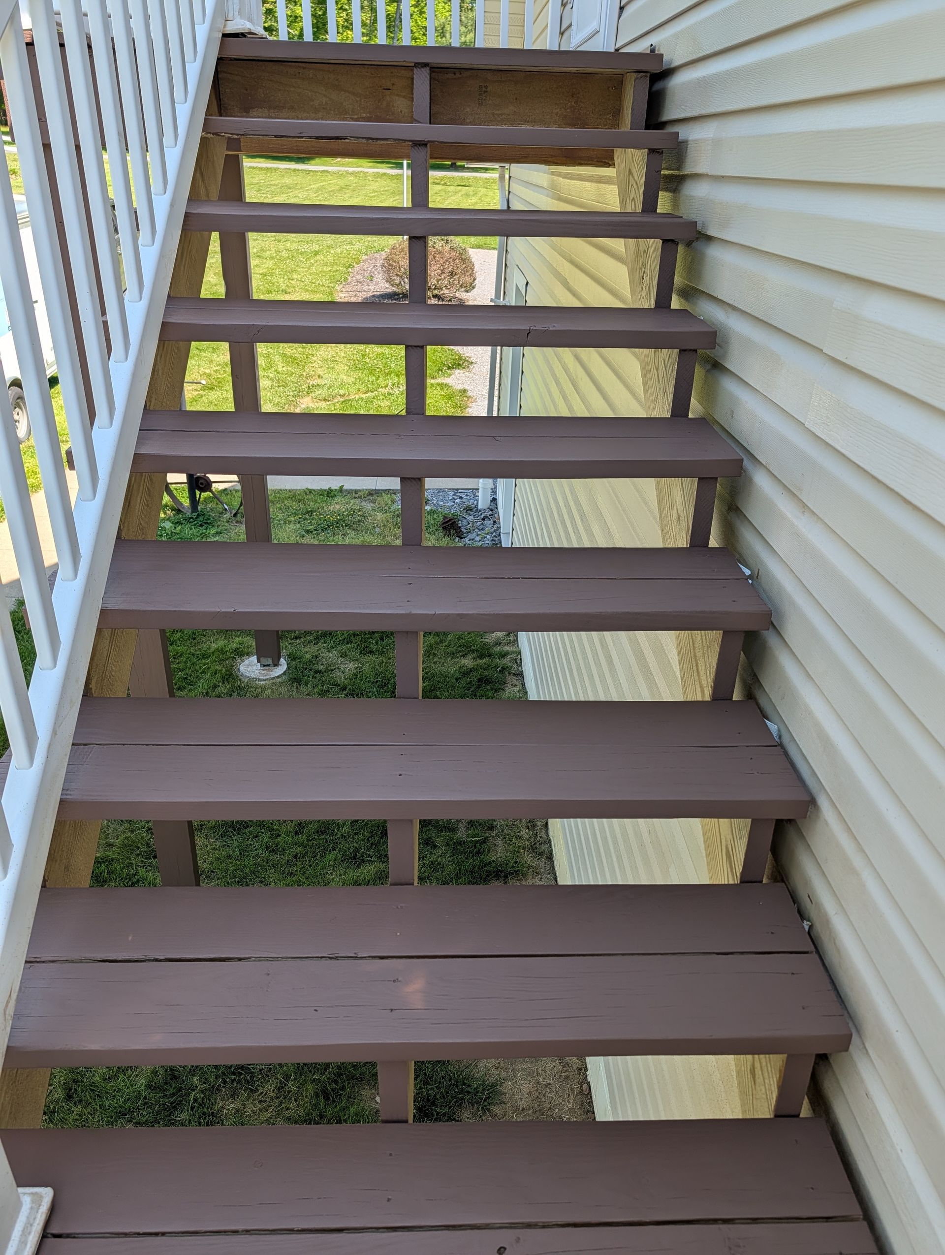 Exterior stairway with brown wooden steps and white railings beside a beige-sided building