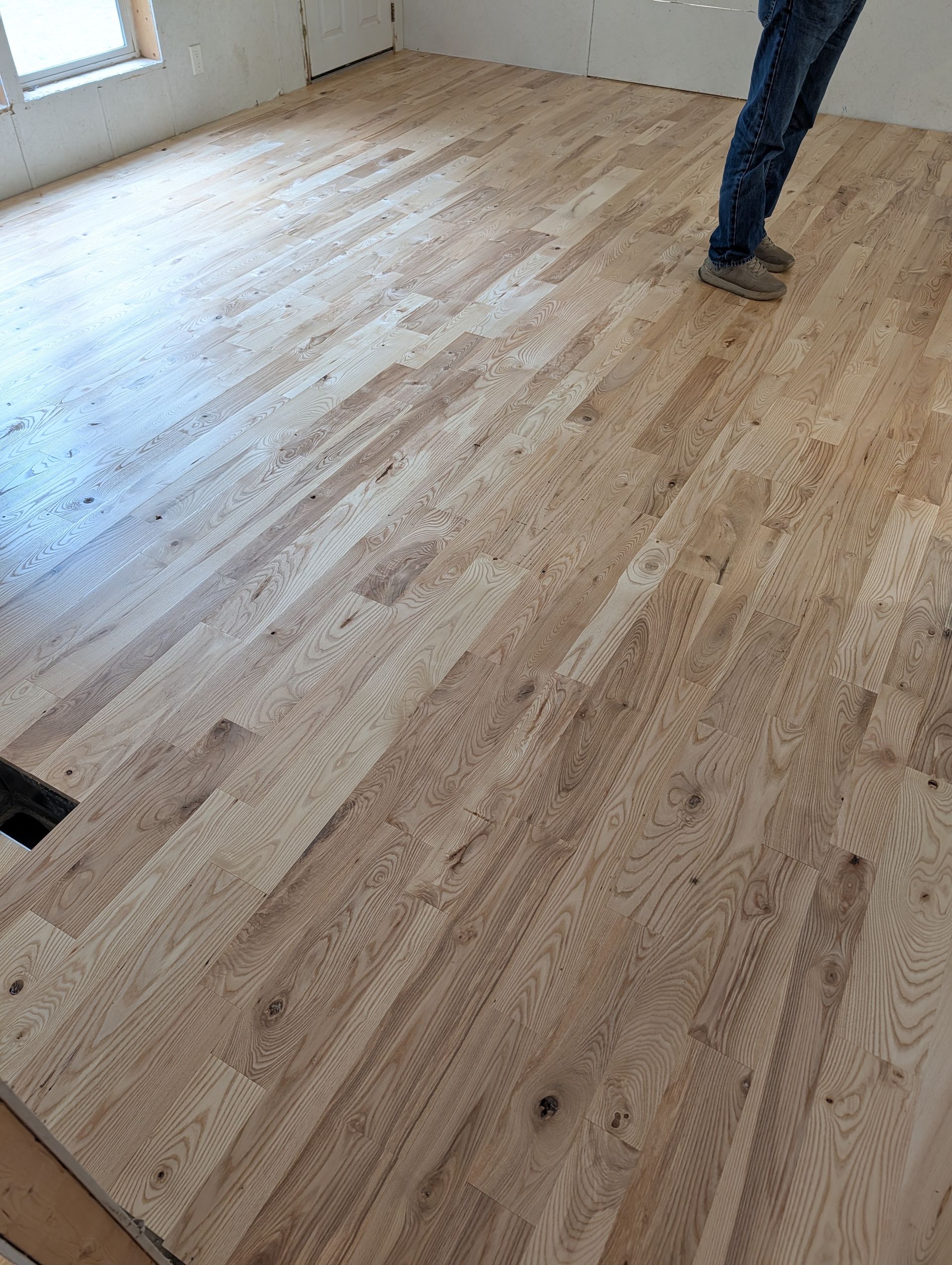 Partially sanded wooden floor in a room with a person standing near a window
