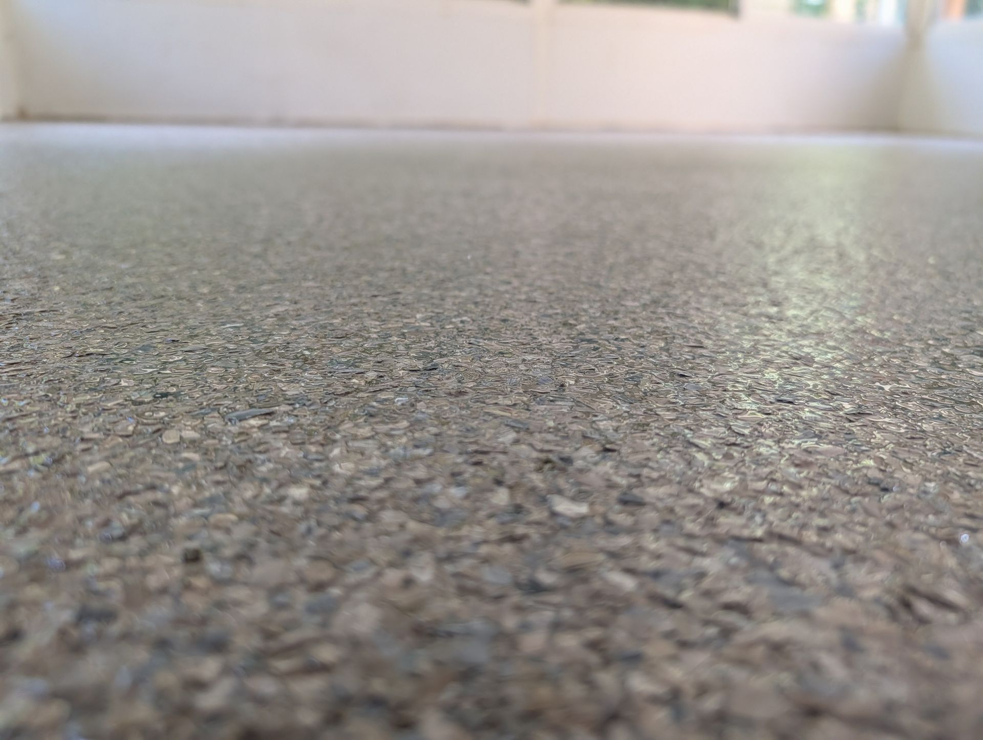 Close-up of a gray, speckled carpet floor with a blurred background and bright light above