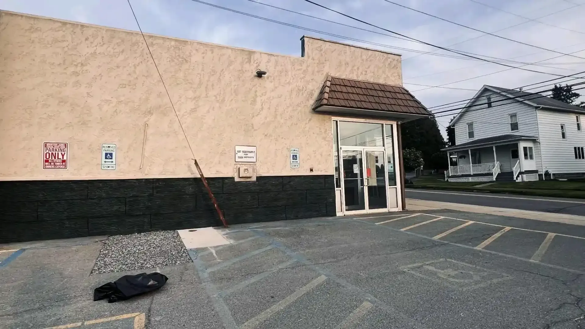 Storefront parking lot with a beige building, glass entrance, and a white house in the background.