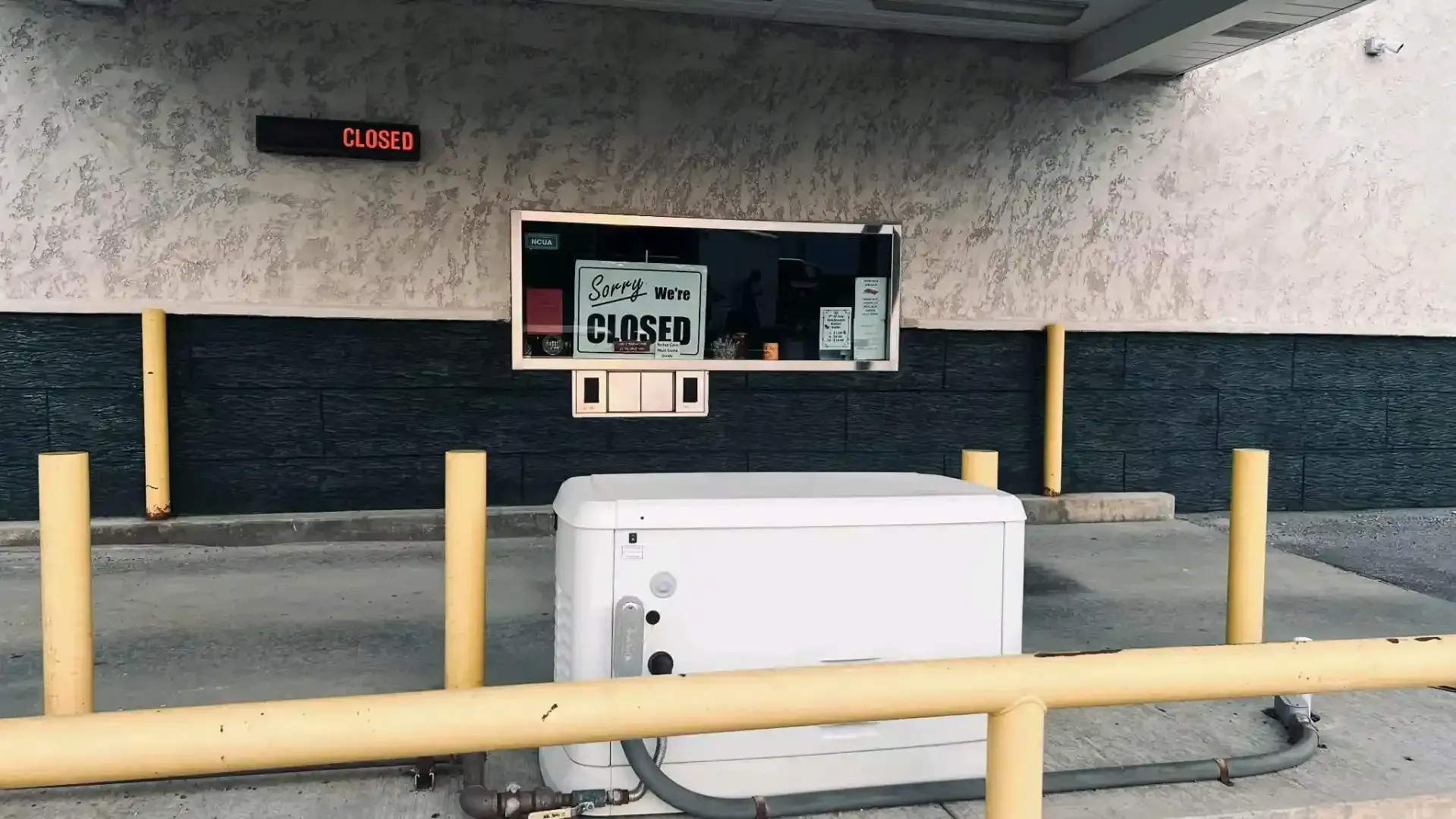 White utility box in a parking area with yellow railings, a wall-mounted sign, and a red digital display.