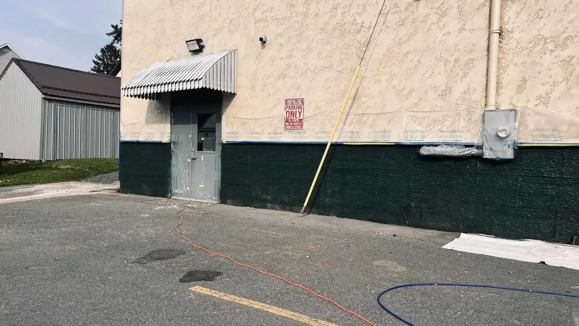 Exterior of a beige building with green lower trim, a metal door awning, and a paved parking area