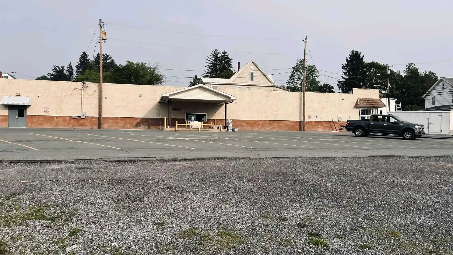 Small beige building with a central entrance, gravel foreground, and a parked black truck on the right.
