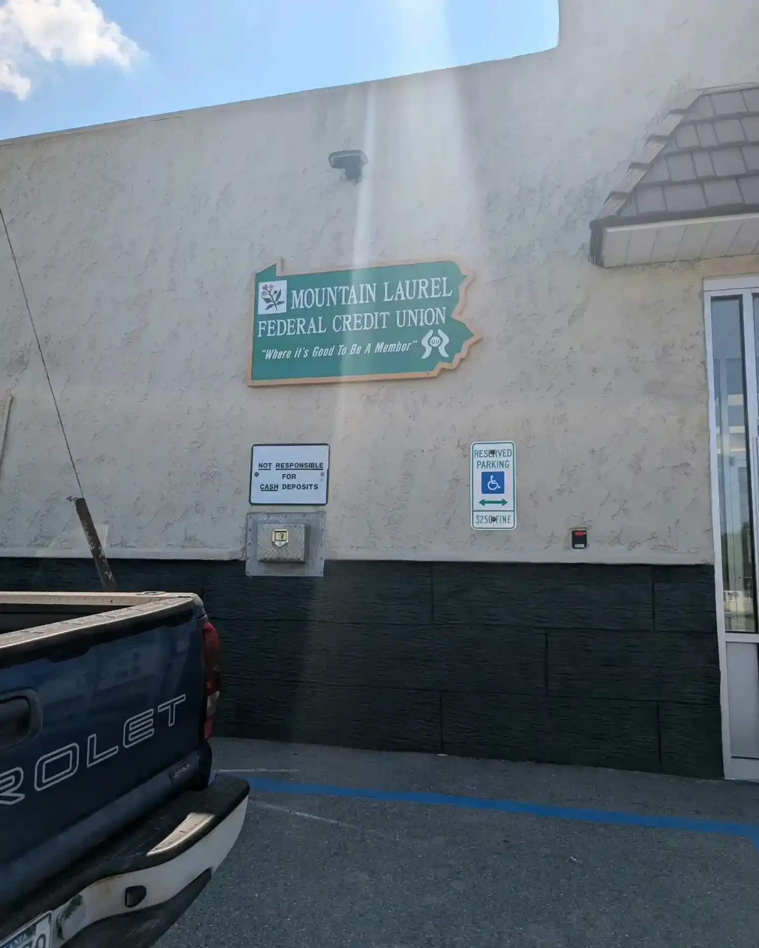 Exterior wall with a green sign for a public library, beside a parked blue pickup truck.