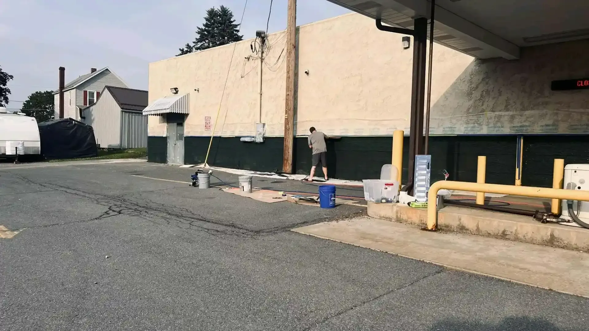 Empty parking lot beside a beige industrial building with yellow barriers and a few bins.