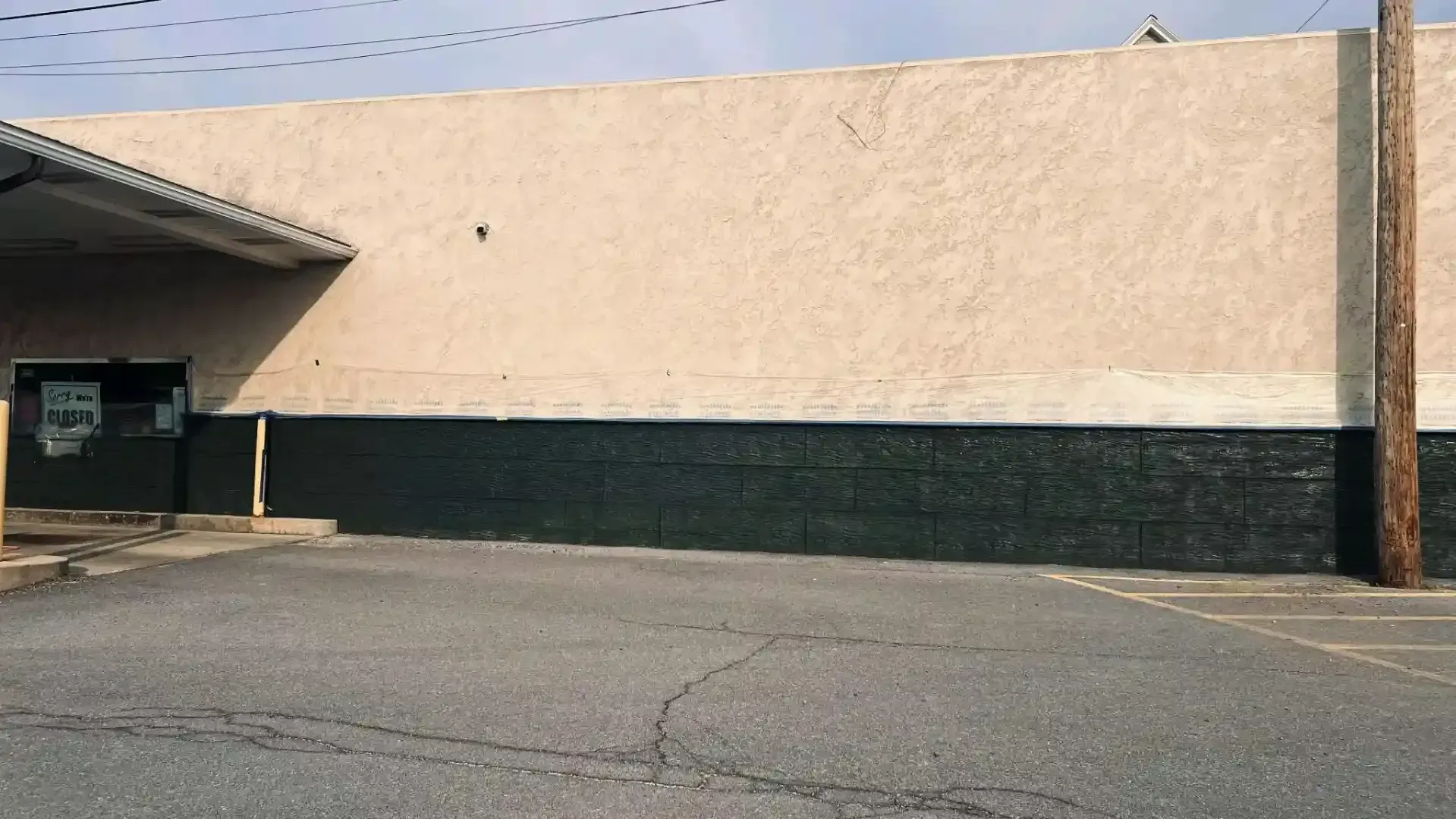Beige building exterior with a dark green base and empty parking lot in front
