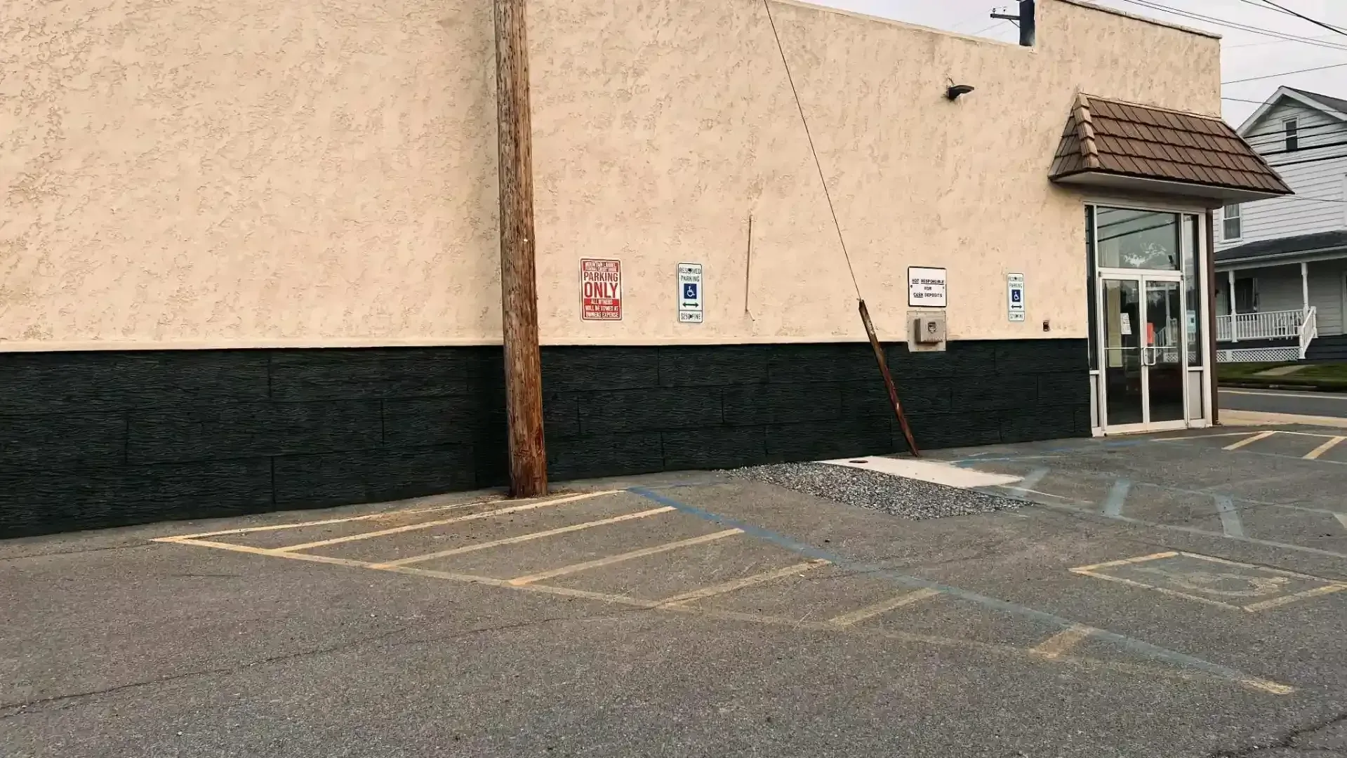 Empty parking lot beside a beige building with yellow painted curb markings and a glass entrance canopy