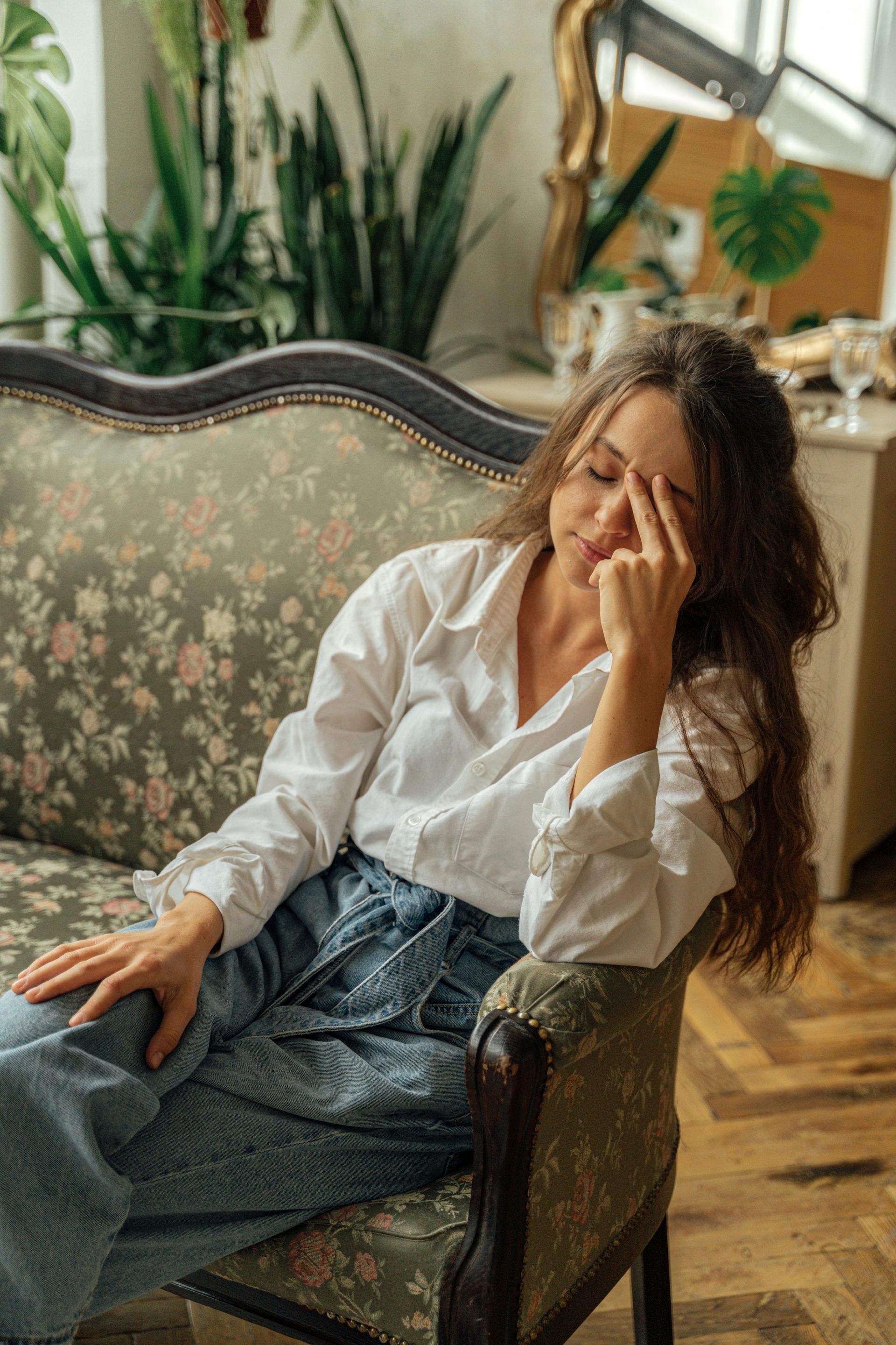 A woman is sitting on a couch covering her face with her hand.