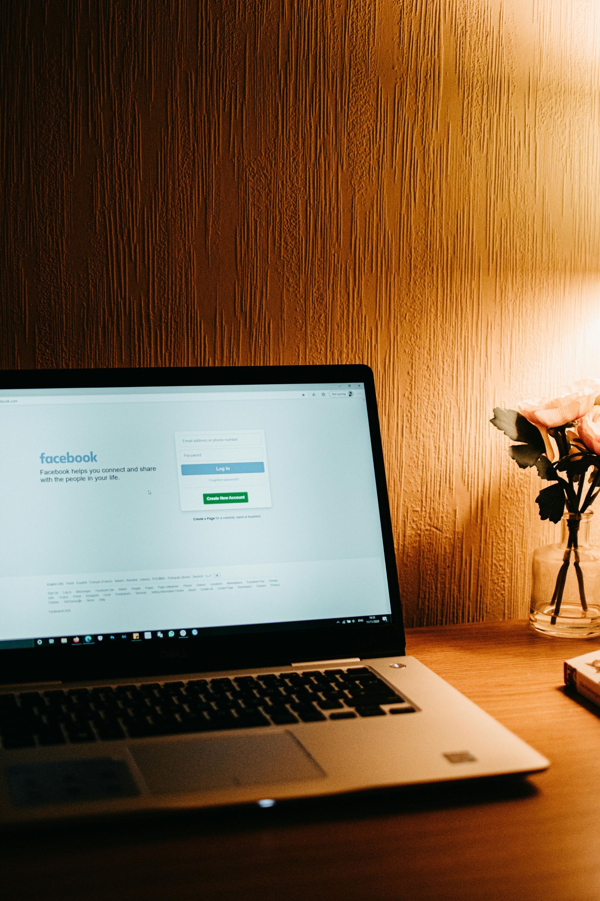 A laptop computer is sitting on a wooden desk next to a vase of flowers.