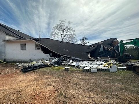 Collapsed house roof with debris scattered across the yard under a cloudy sky