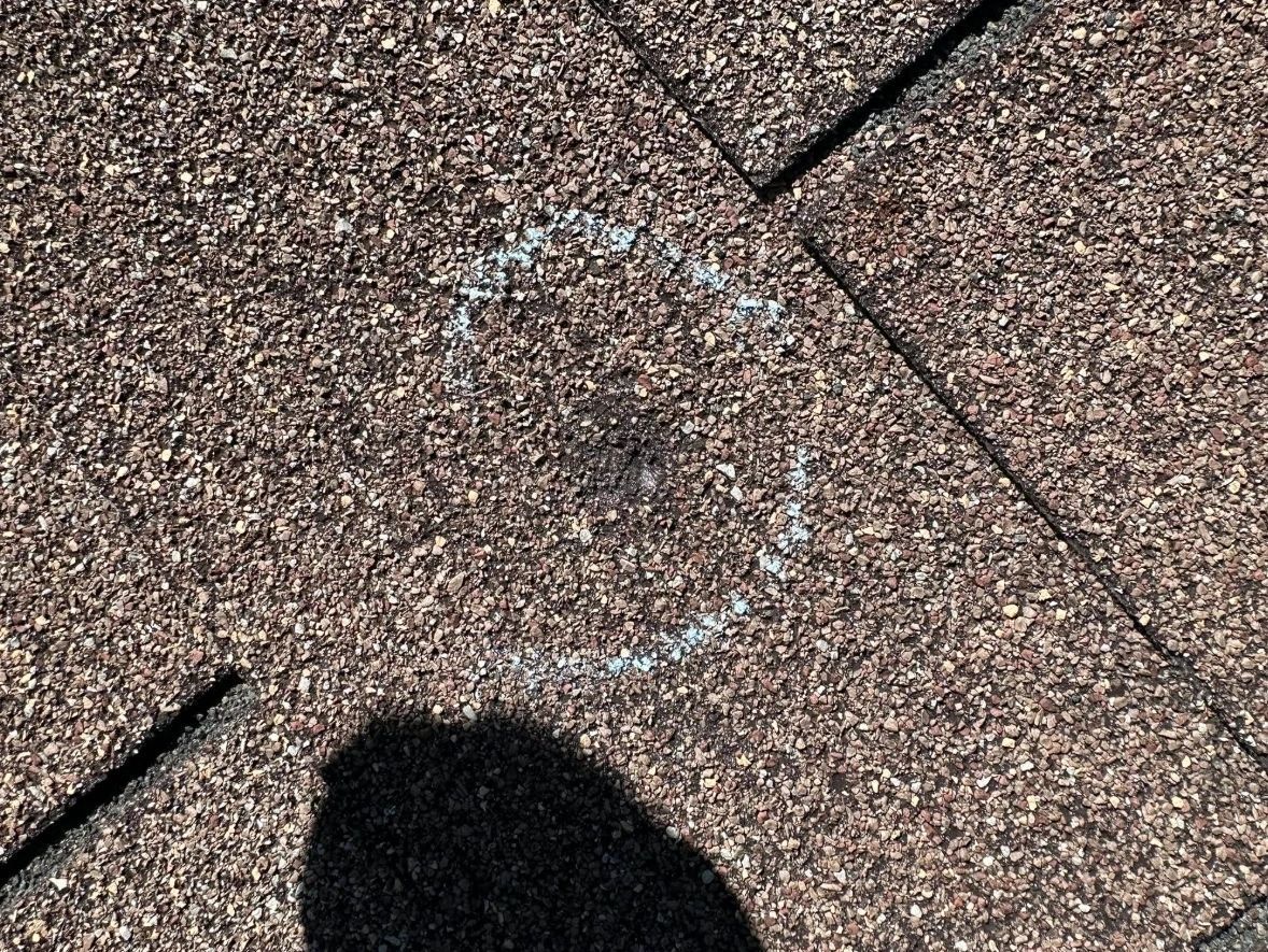 Close-up of brown asphalt shingles with a faint white chalk marking and a dark shadow at bottom left