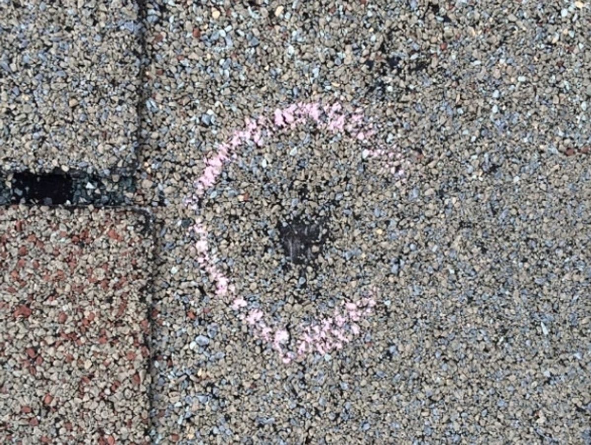 Pink chalk circle on a gray concrete surface next to a dark crack and faded painted line