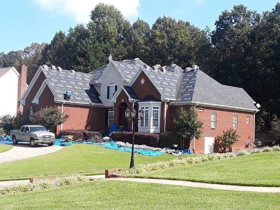 Suburban brick house with gray roof, front lawn, driveway, and parked car under trees