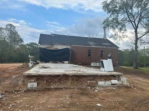 Damaged brick house with a collapsed front porch and debris in a muddy yard