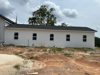 Single-story white building on bare dirt lot under cloudy sky
