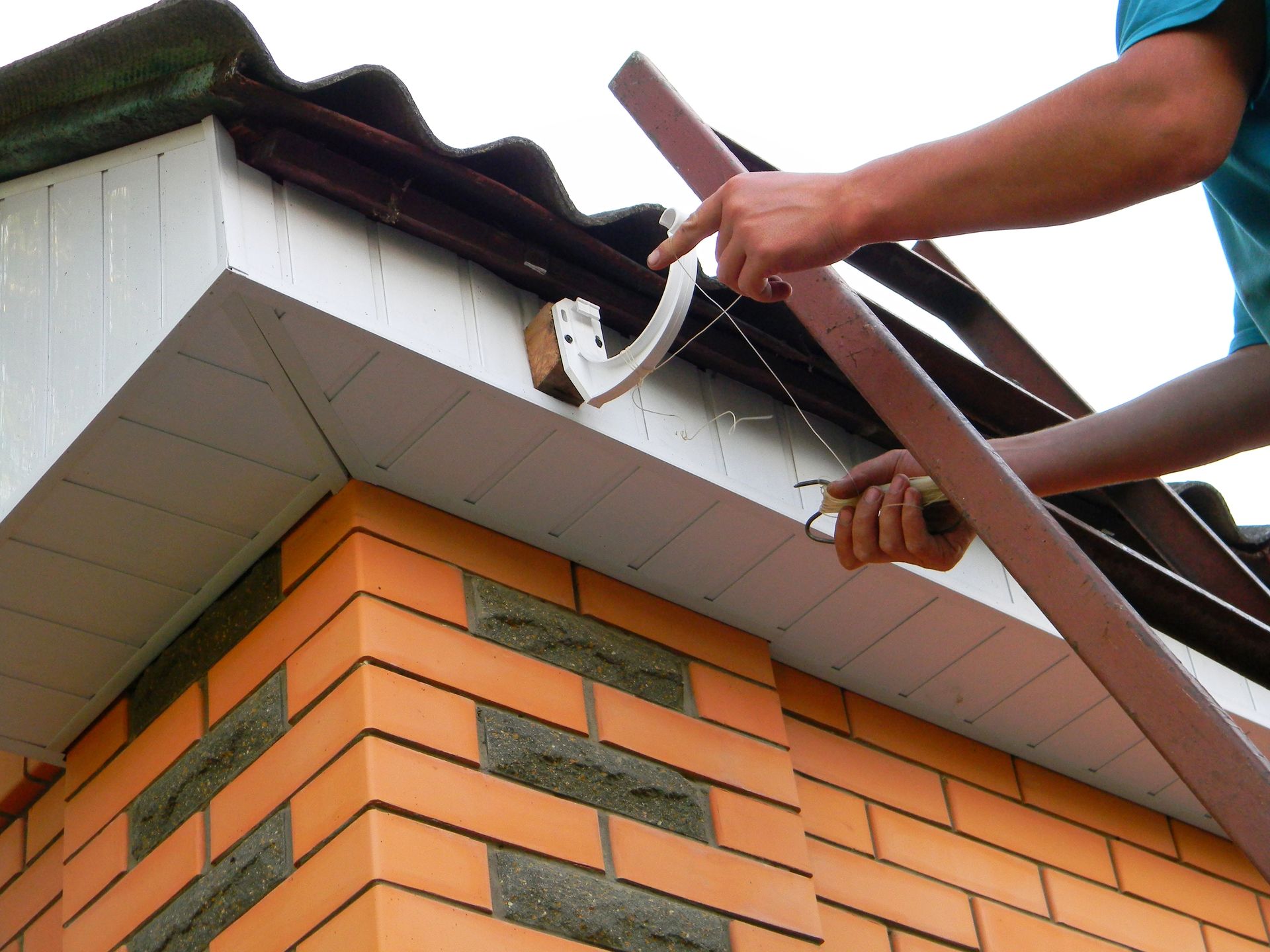 Worker installing gutter on brick house roof edge