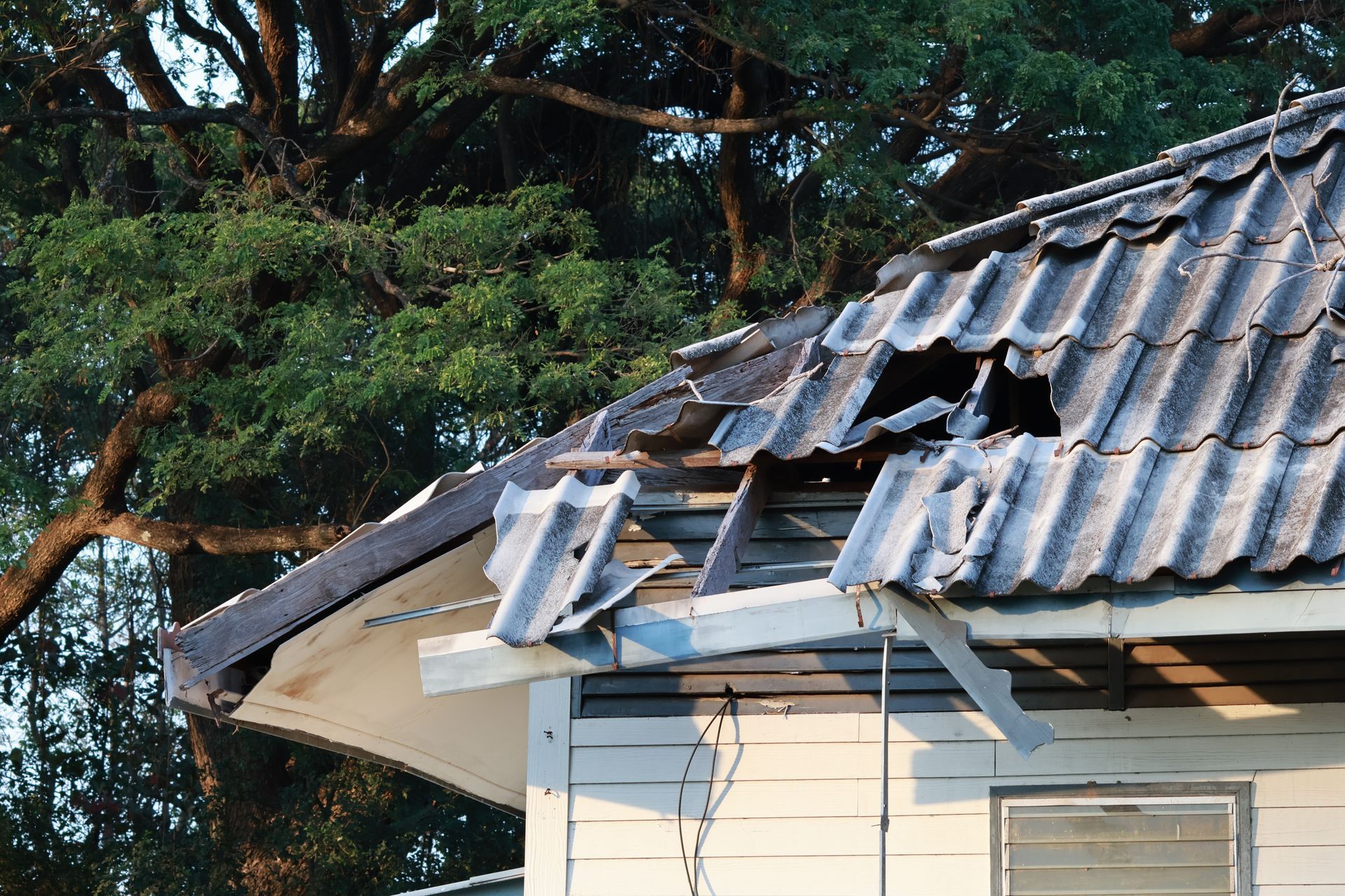Damaged tiled roof with broken panels on a house, with trees in the background