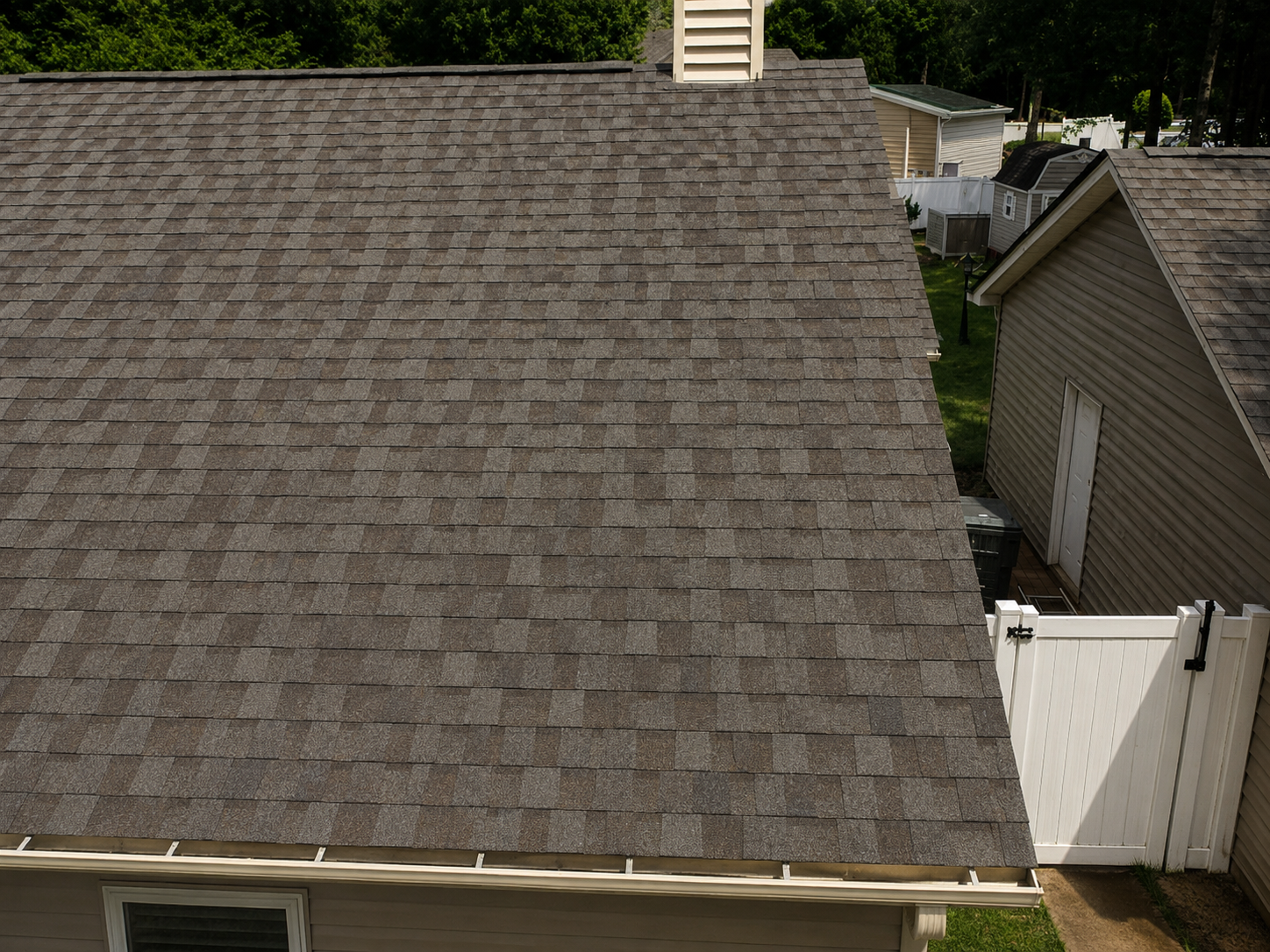 Gray shingled roof of a house with trees and neighboring homes in the background
