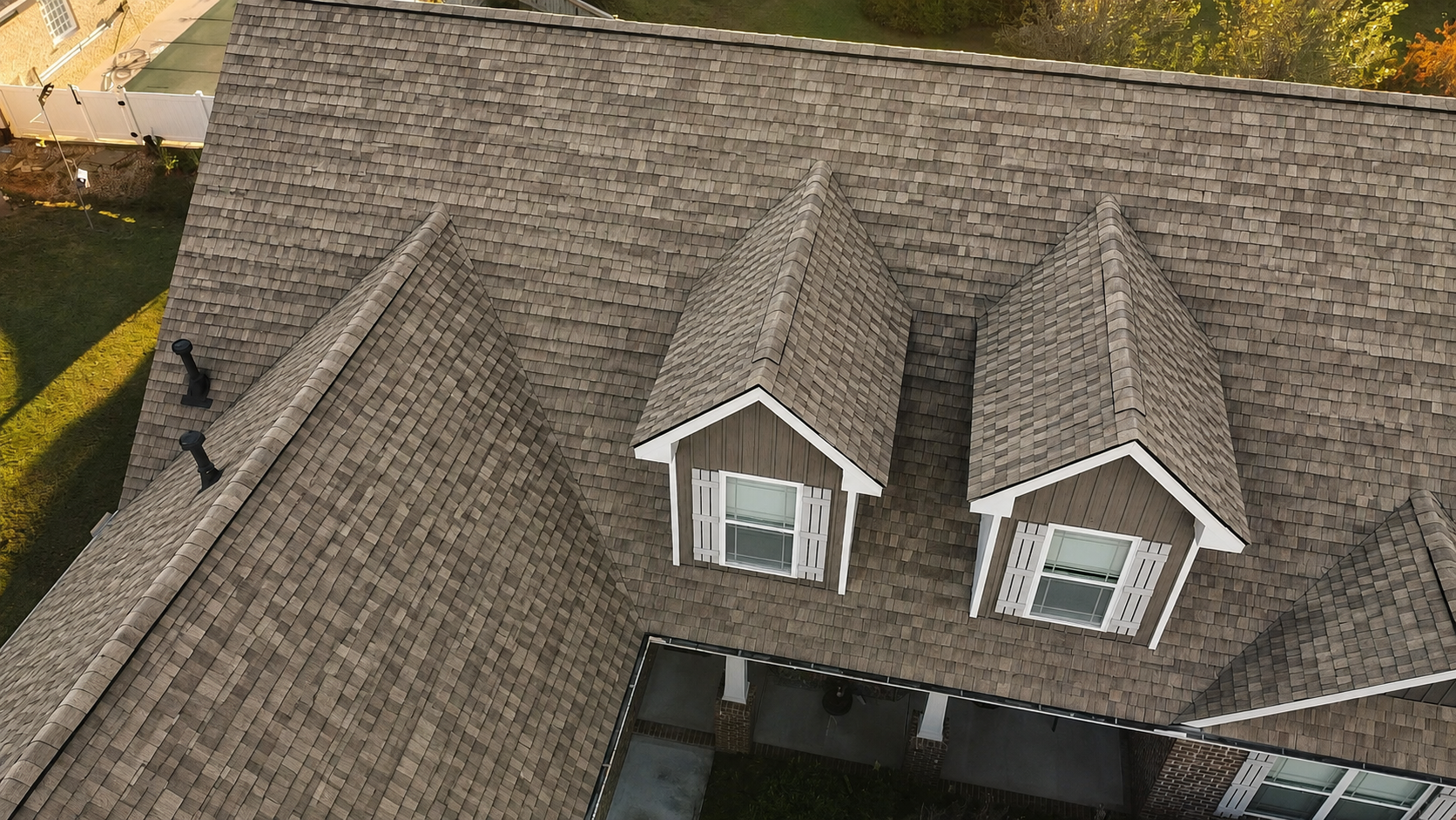 Aerial view of a gray shingled roof with two white dormer windows.