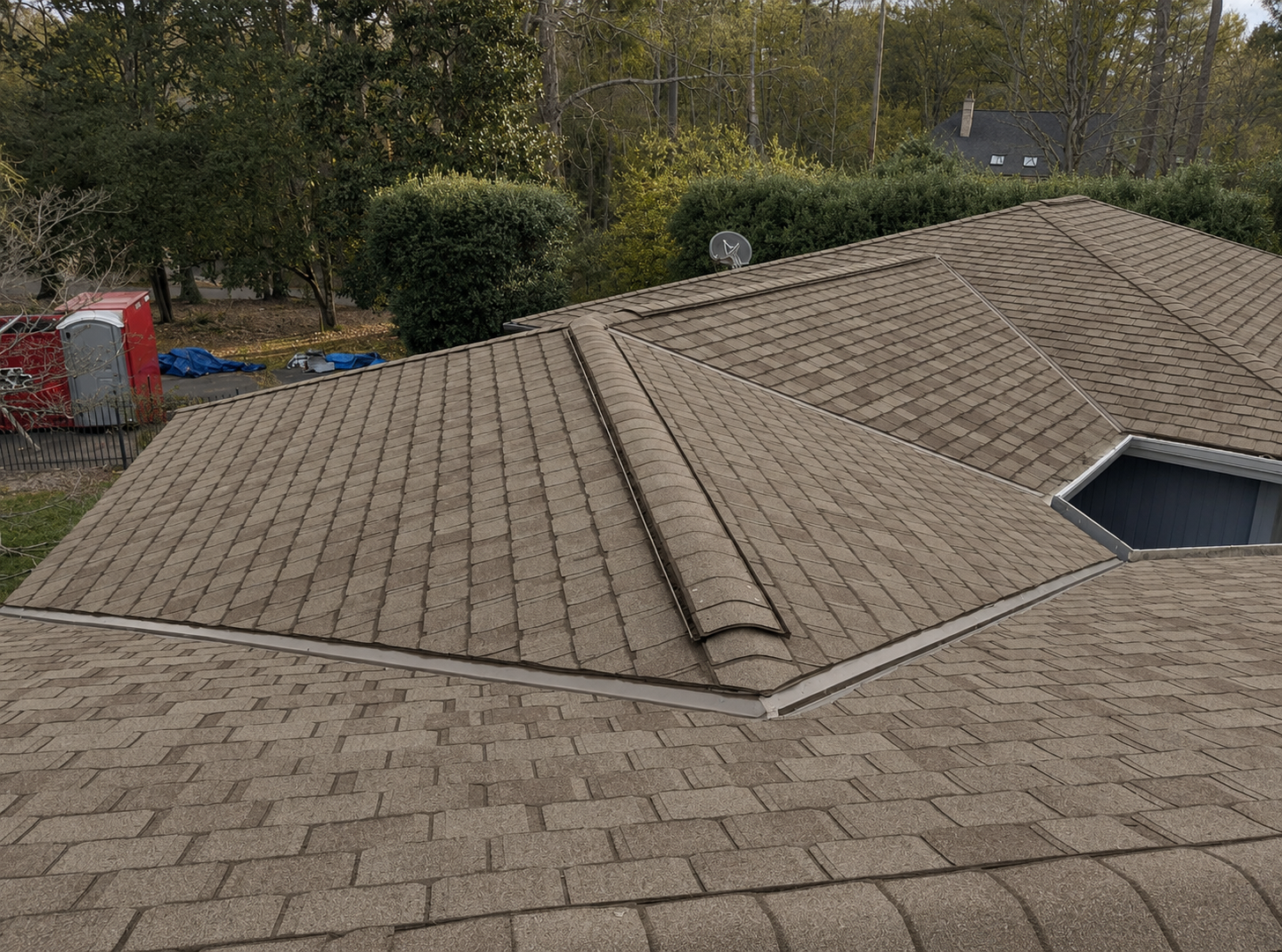 Roof under construction with gray shingles and workers near a skylight opening