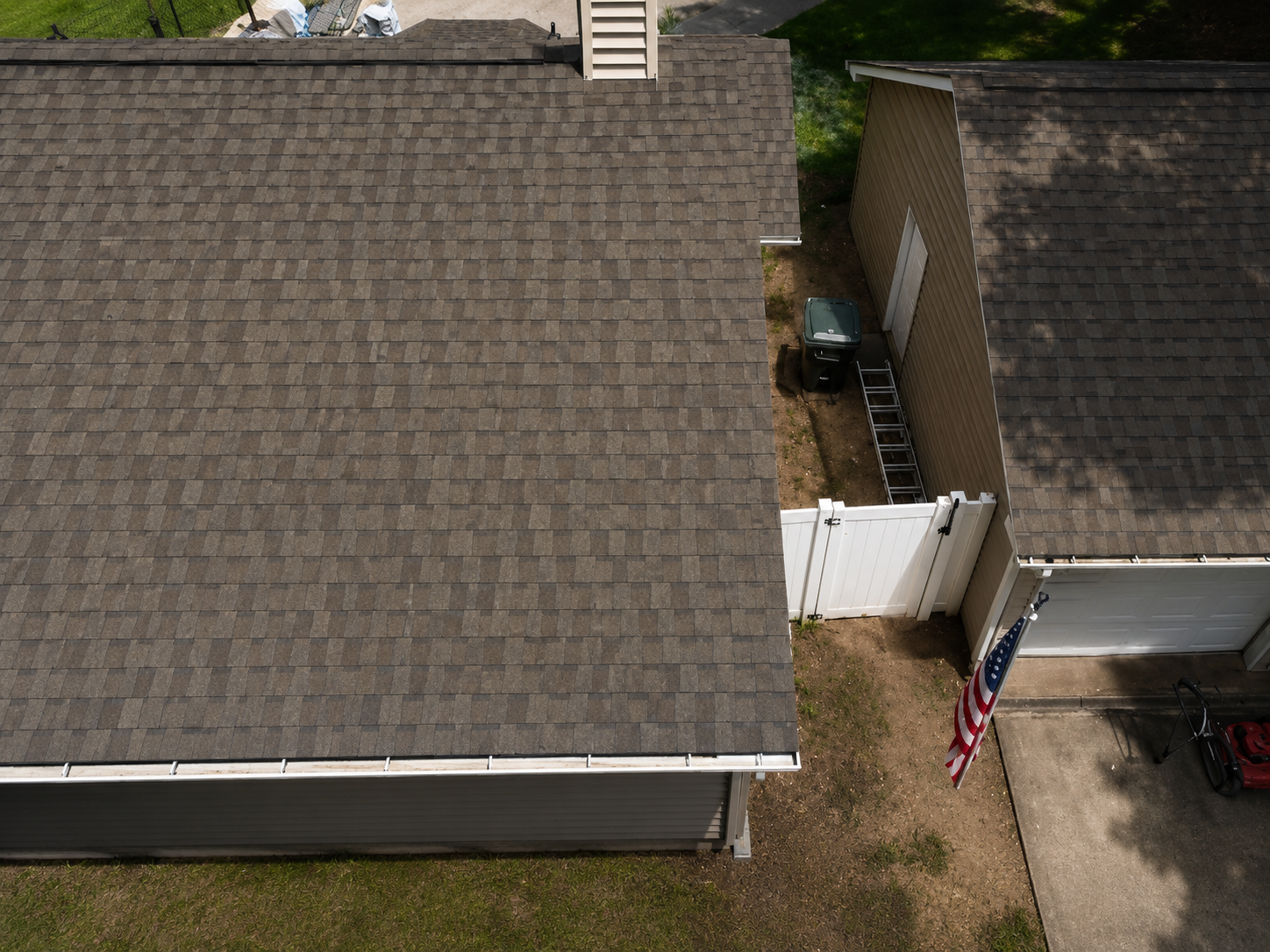 Aerial view of two neighboring houses with gray shingle roofs and a white fence between them.