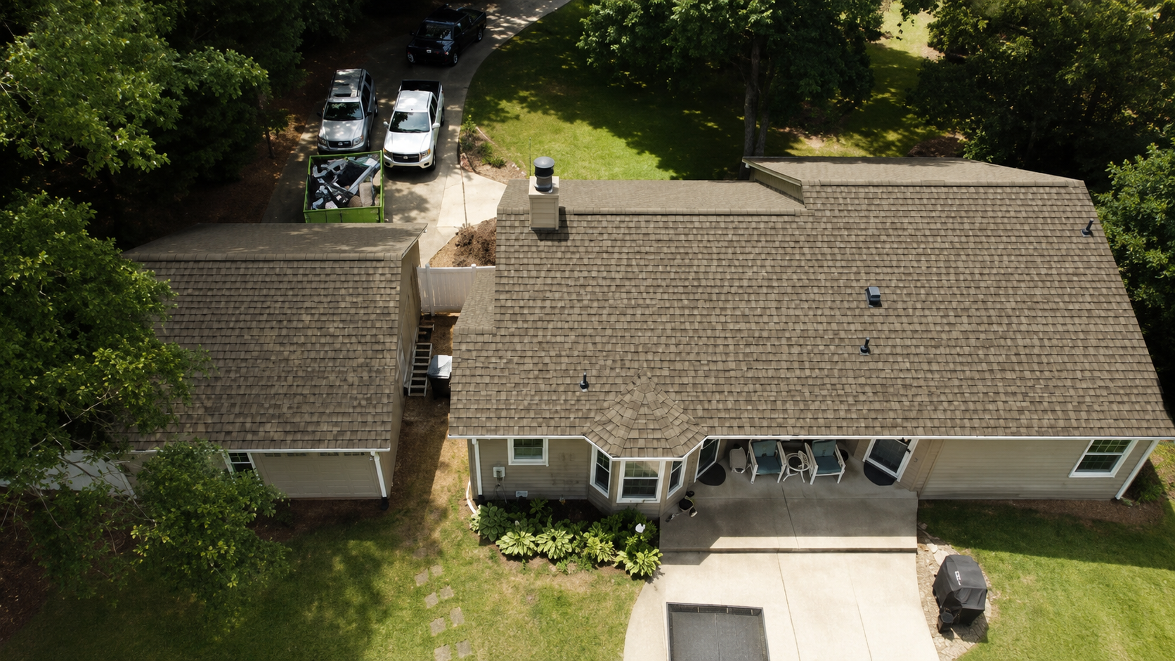 Aerial view of two houses with a driveway, parked cars, and trees around the property.