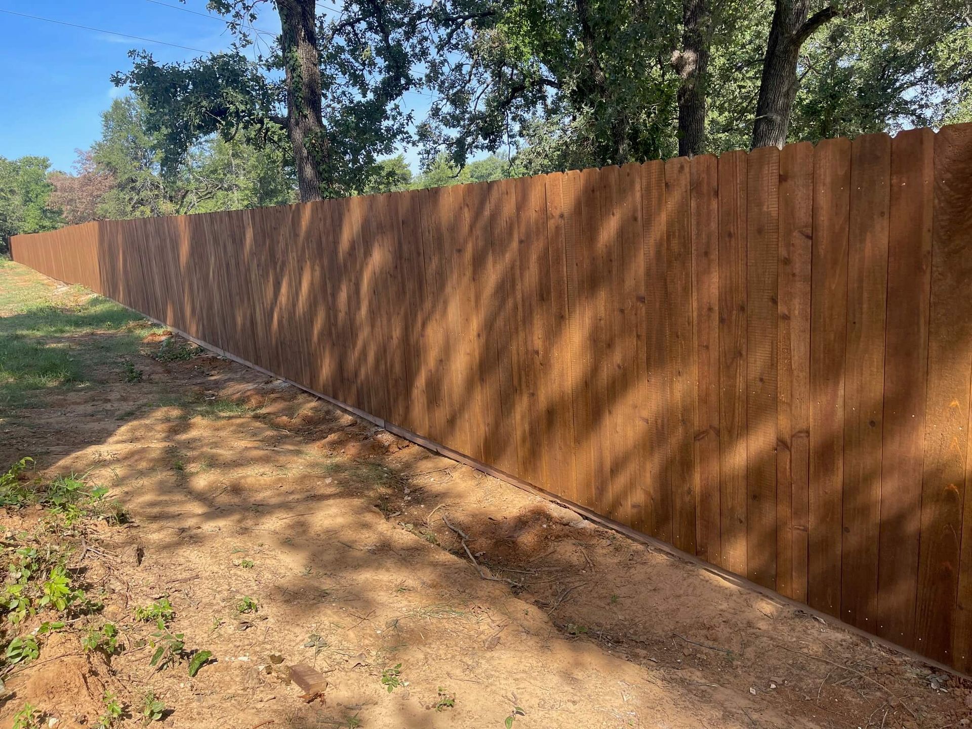 A Wooden Fence Surrounds a Dirt Field with Trees in The Background