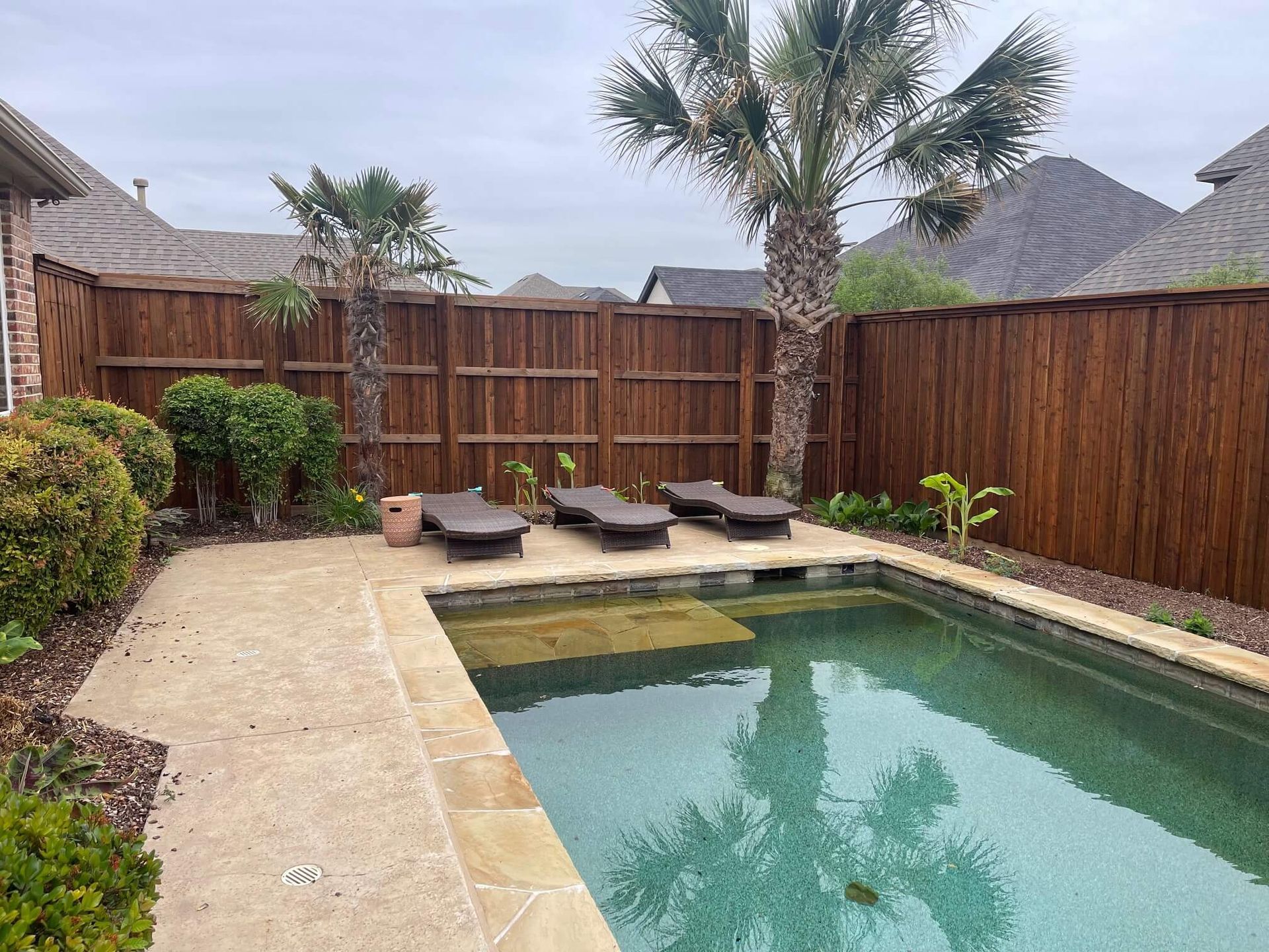 A Large Swimming Pool Surrounded by A Wooden Fence and Palm Trees