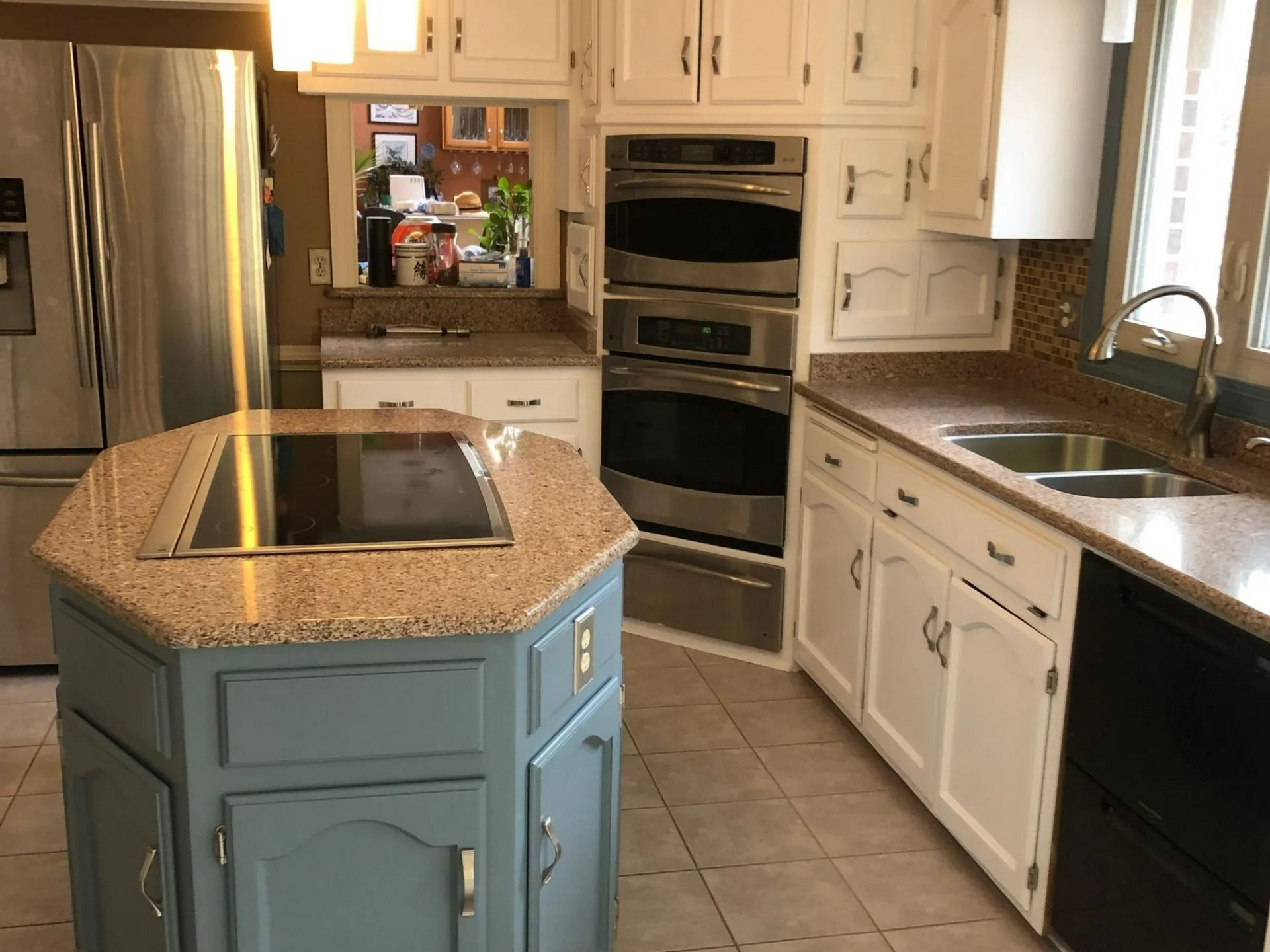 Kitchen with blue island, stainless steel appliances, white cabinets, and speckled countertops.