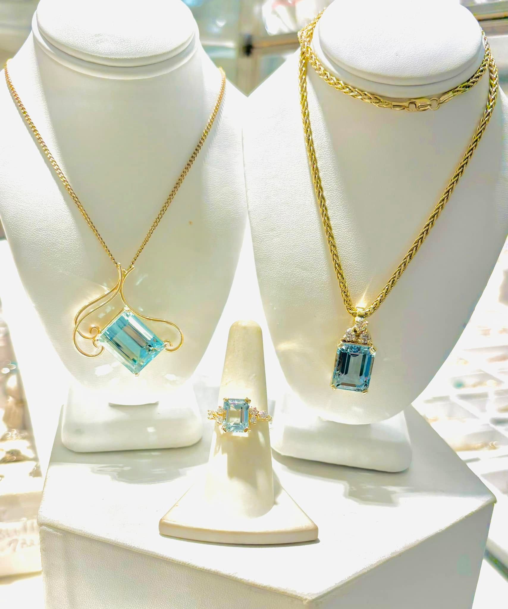 Gold necklaces with blue gemstone pendants displayed on white jewelry stands, with matching ring and bracelet.