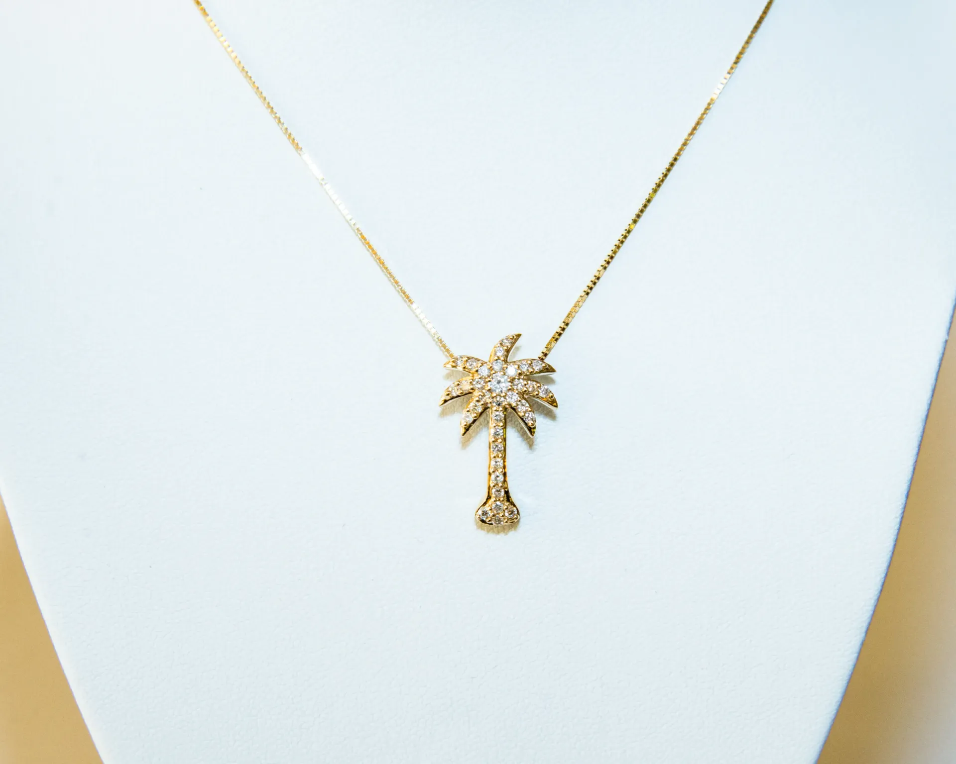 Gold palm tree pendant necklace on a white display bust.