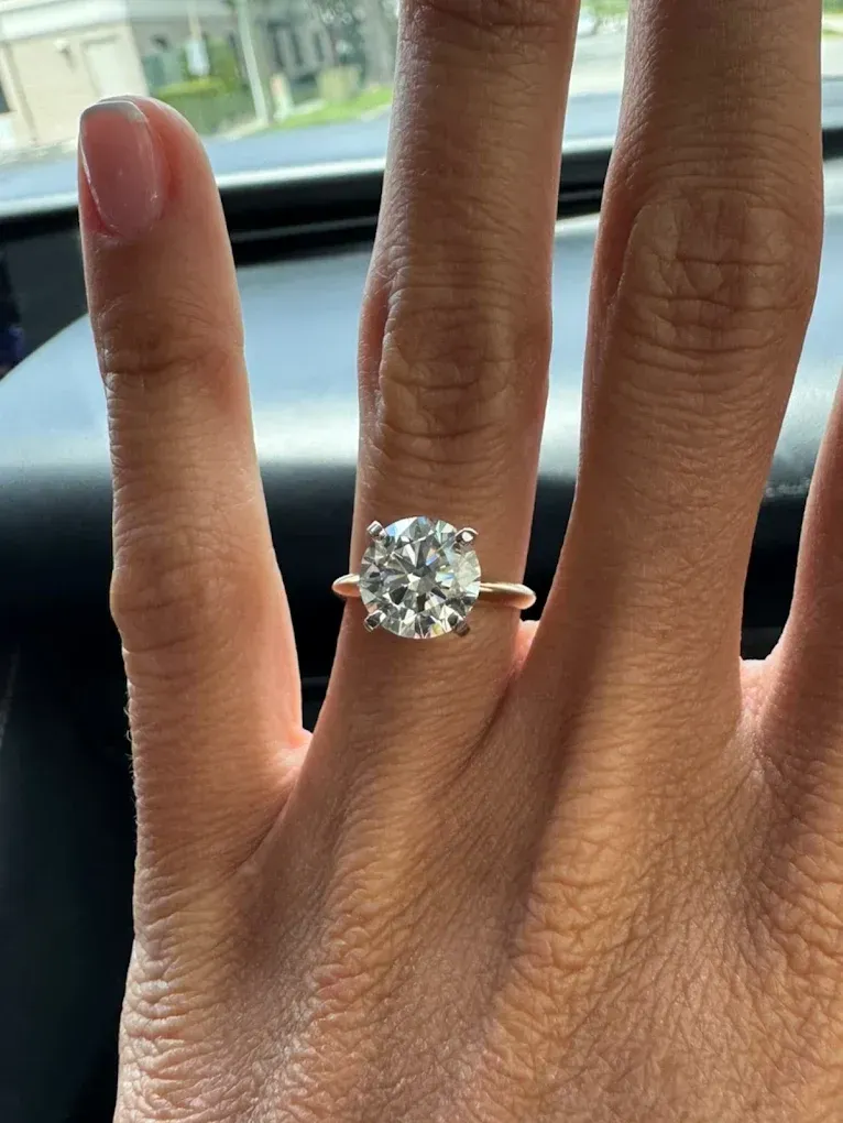 Hand with a large diamond ring, shown against a car window background.