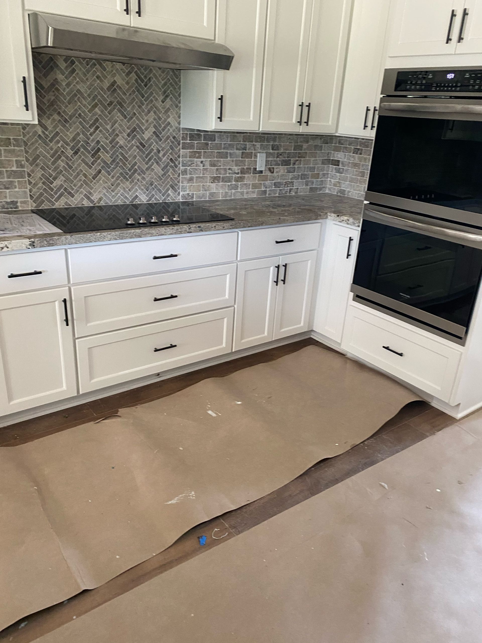 White kitchen cabinets, granite countertops, stainless steel appliances, and a herringbone backsplash.