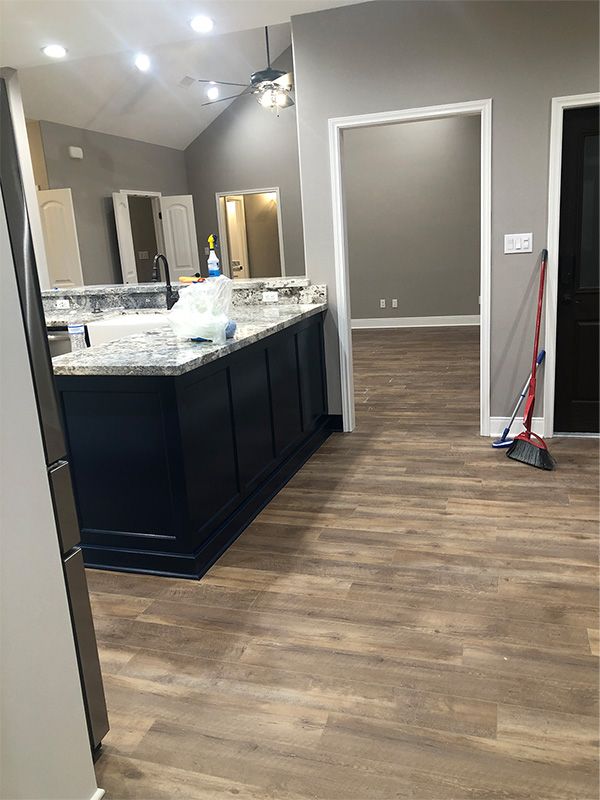 Kitchen with dark island, granite countertop, and wood-look flooring. Doorways lead to other rooms.