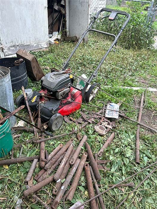 A lawnmower sits in a yard with scattered metal debris.