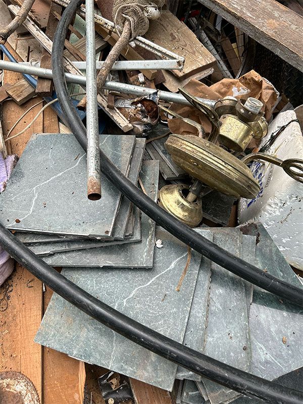 Pile of construction debris: grey tiles, black rubber tubing, metal pipes, brass light fixtures, and wood.