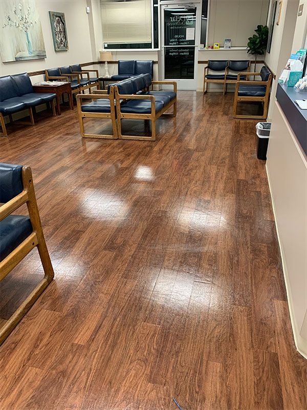Waiting room with brown wood-look floors, blue chairs, and a reception desk.