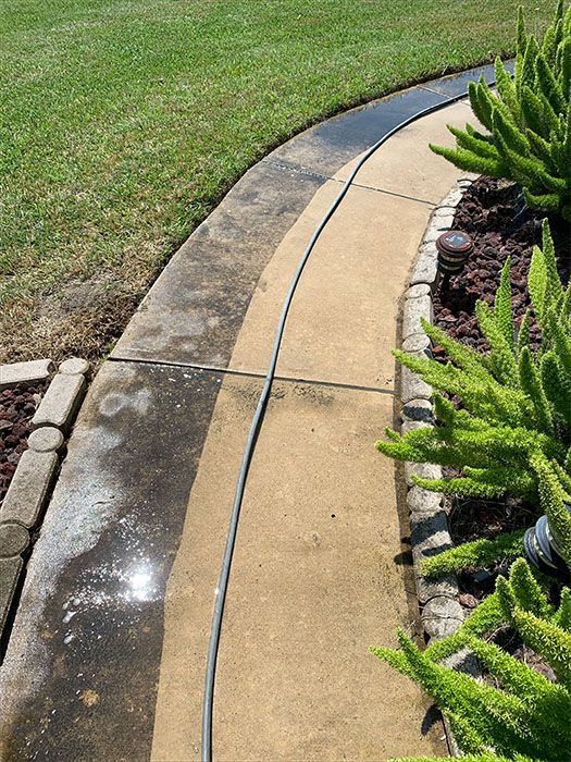 A concrete walkway being power washed; showing before and after cleaning.