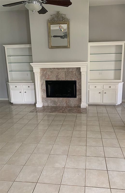Living room with fireplace, white built-in shelving, gold-framed mirror, and tile floor.
