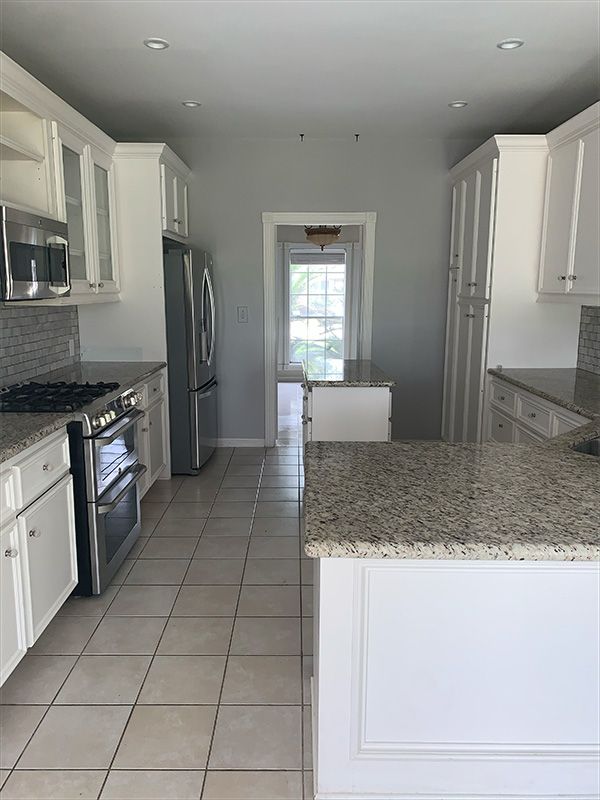White kitchen with stainless steel appliances, granite countertops, and gray walls.