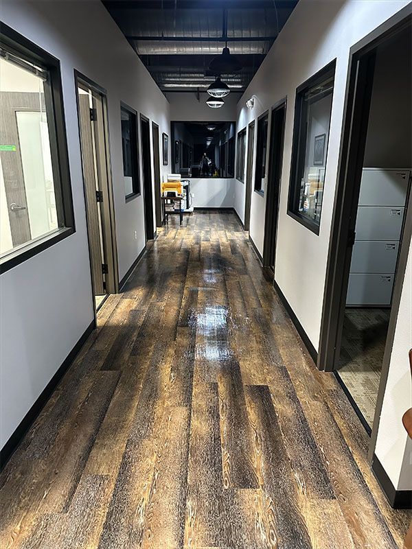 Long hallway with wood-look flooring, windows, and doors on both sides; overhead lights.