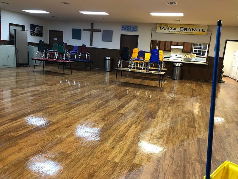 Empty room with hardwood floors, chairs stacked on tables, and a cross on the wall.