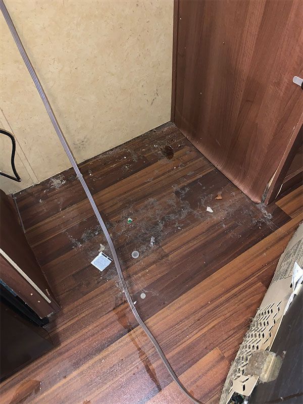 Dirty floor corner with wood-look laminate, cables, debris and brown wood cabinetry.
